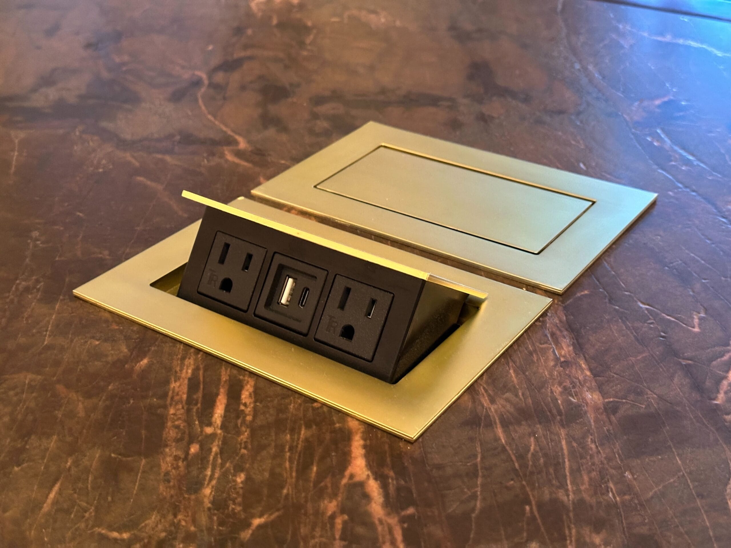A pop-up outlet with two power sockets and USB ports, set in brass on marble—perfect for a luxury hotel like Grand Floridian.