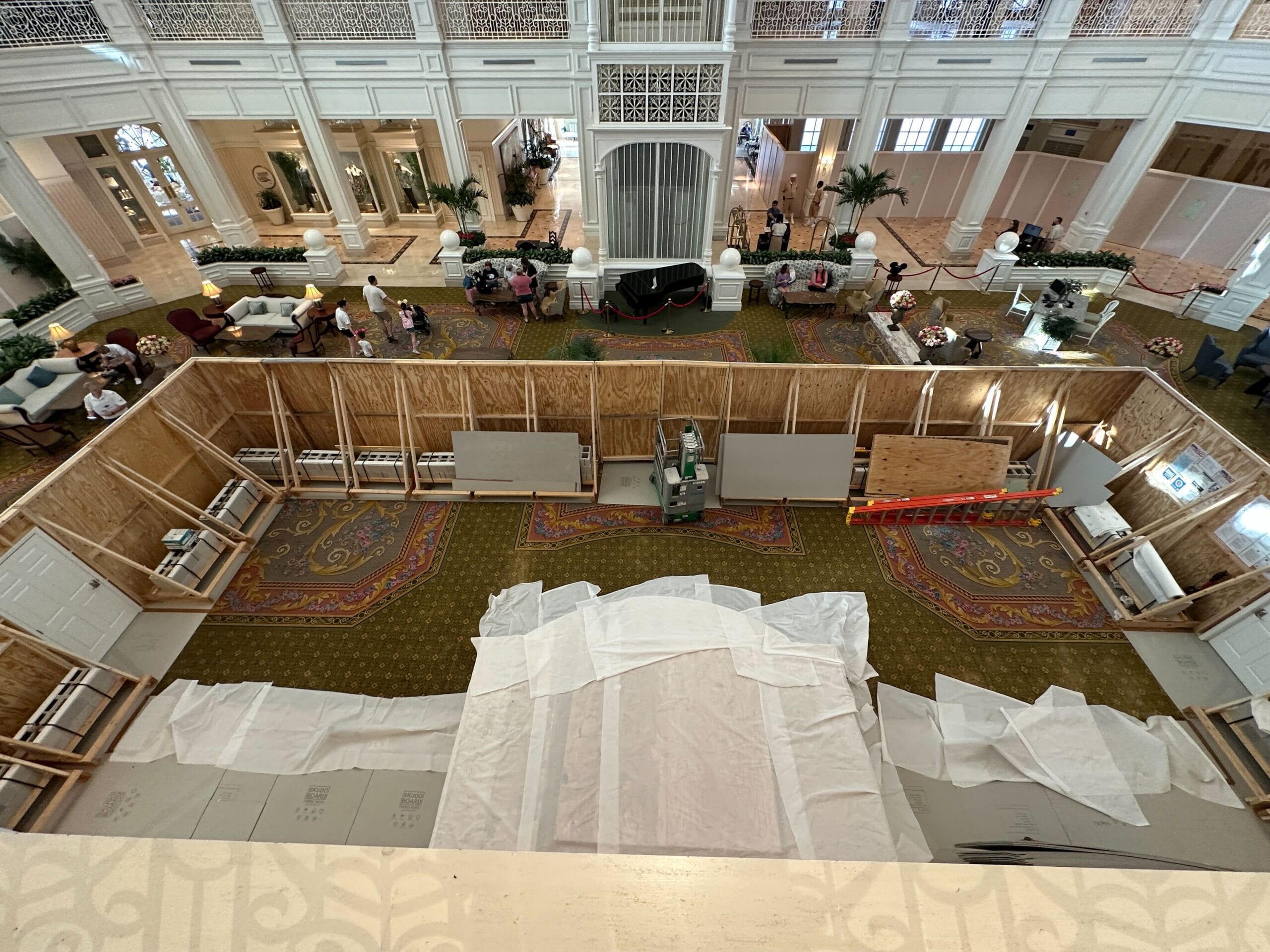 Hotel lobby with a large wooden construction area, white sheets, people nearby, and H2O Glow After Hours food stands.
