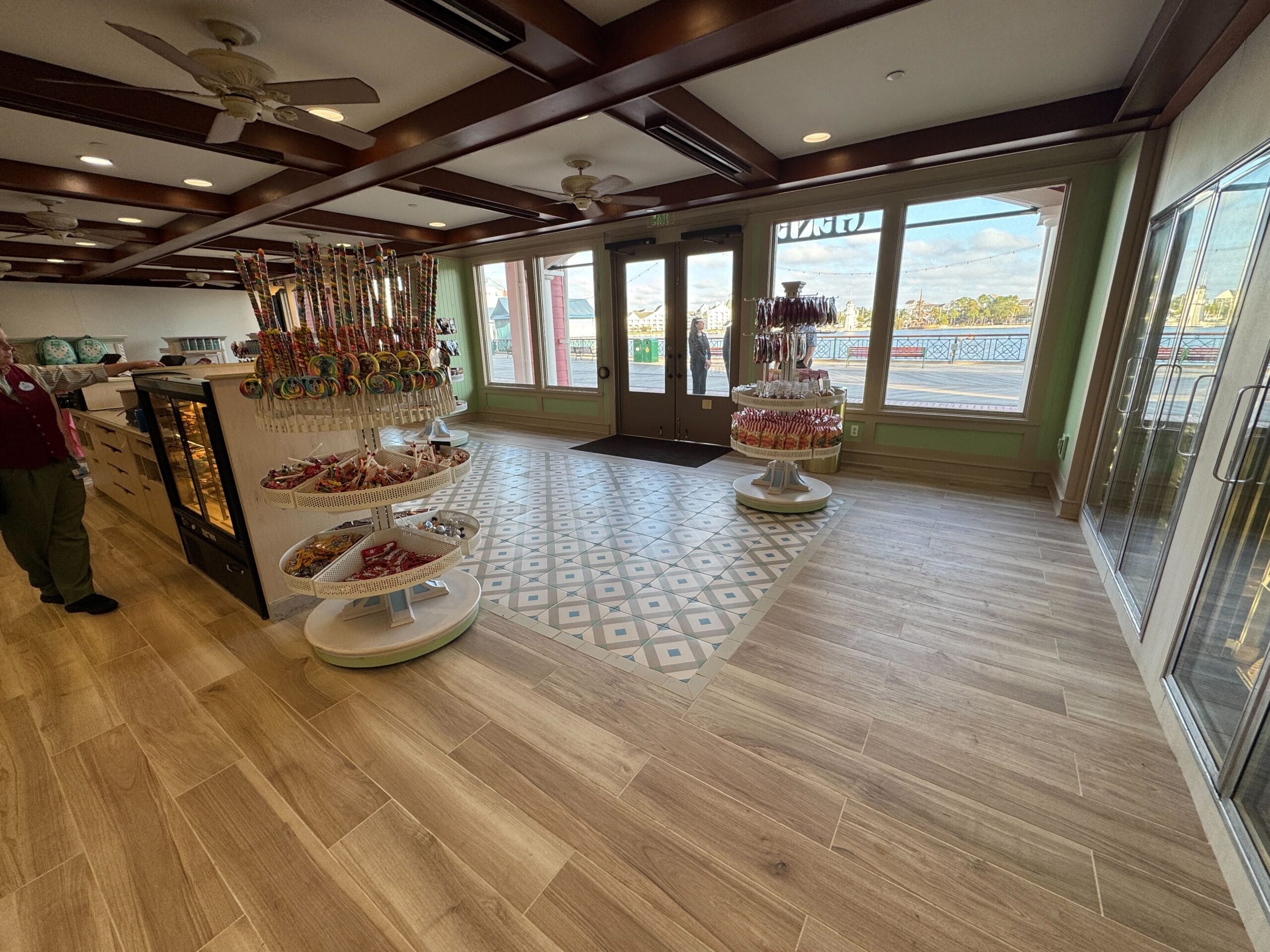 A candy store interior with displays of sweets on shelves and tables. Large windows and glass door let in natural light.