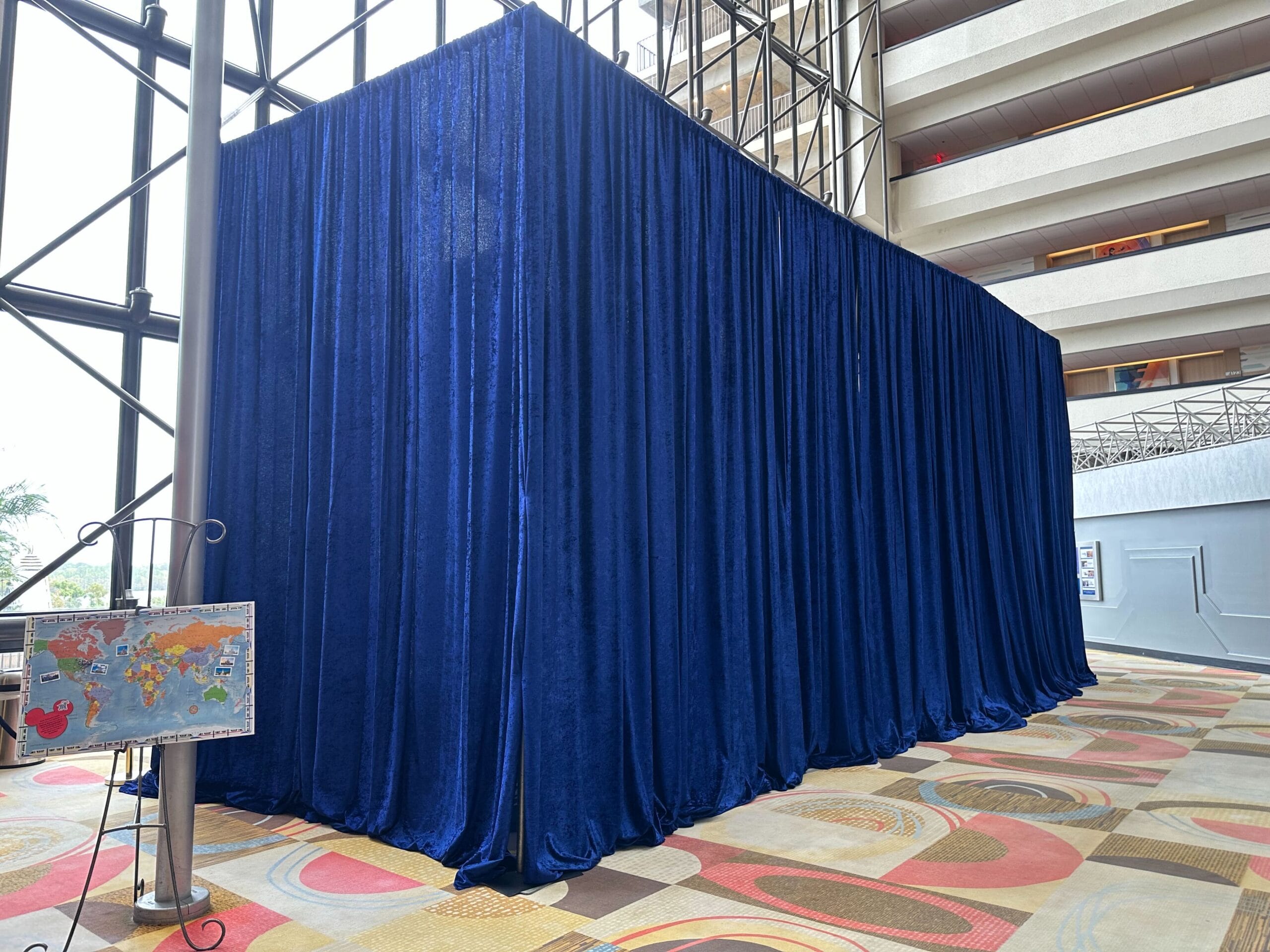A large blue curtain in a spacious lobby, covering a structure, with a world map on a stand nearby.