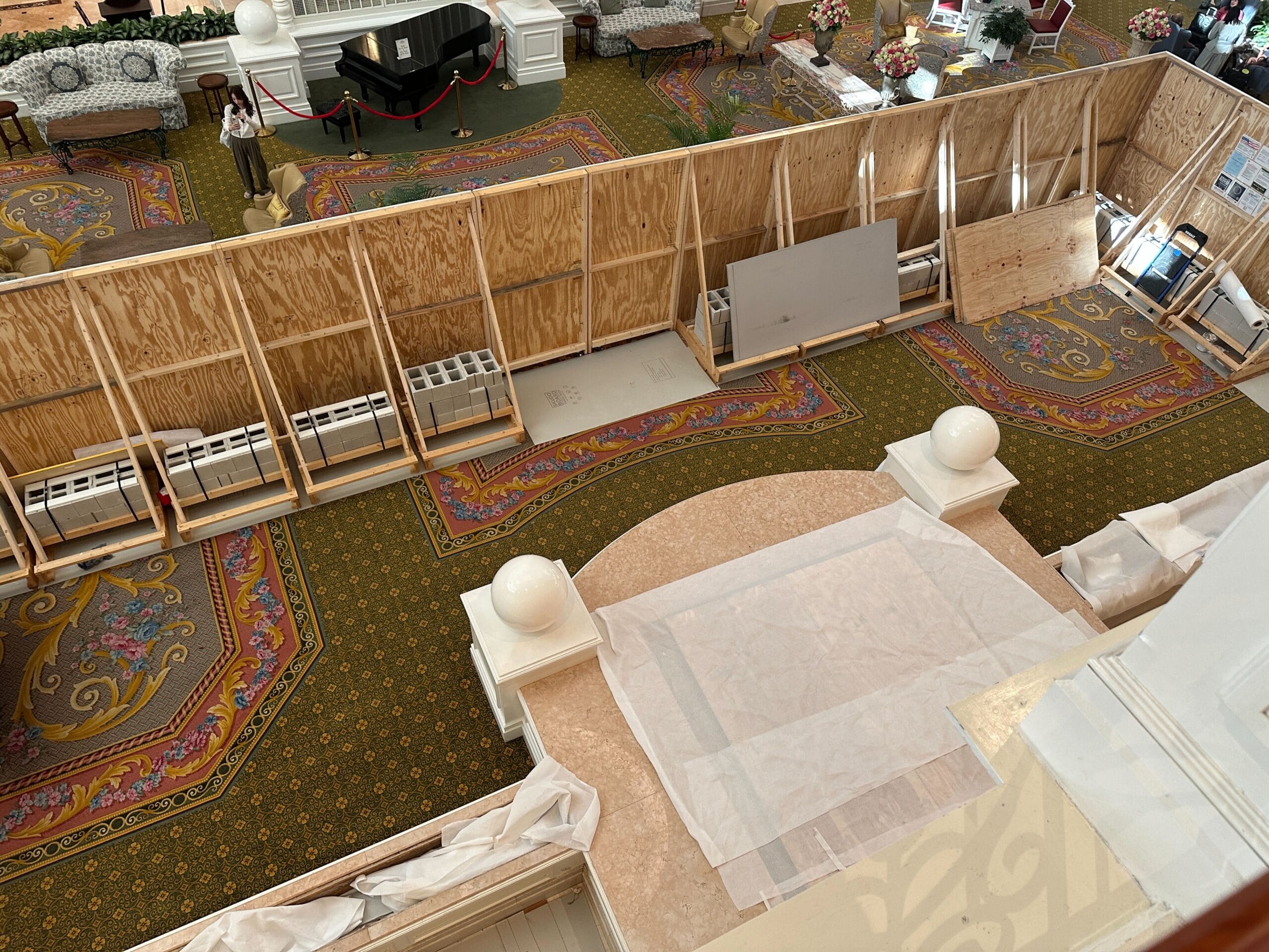 View of a hotel lobby under renovation with wooden barriers, covered floors, and construction materials.