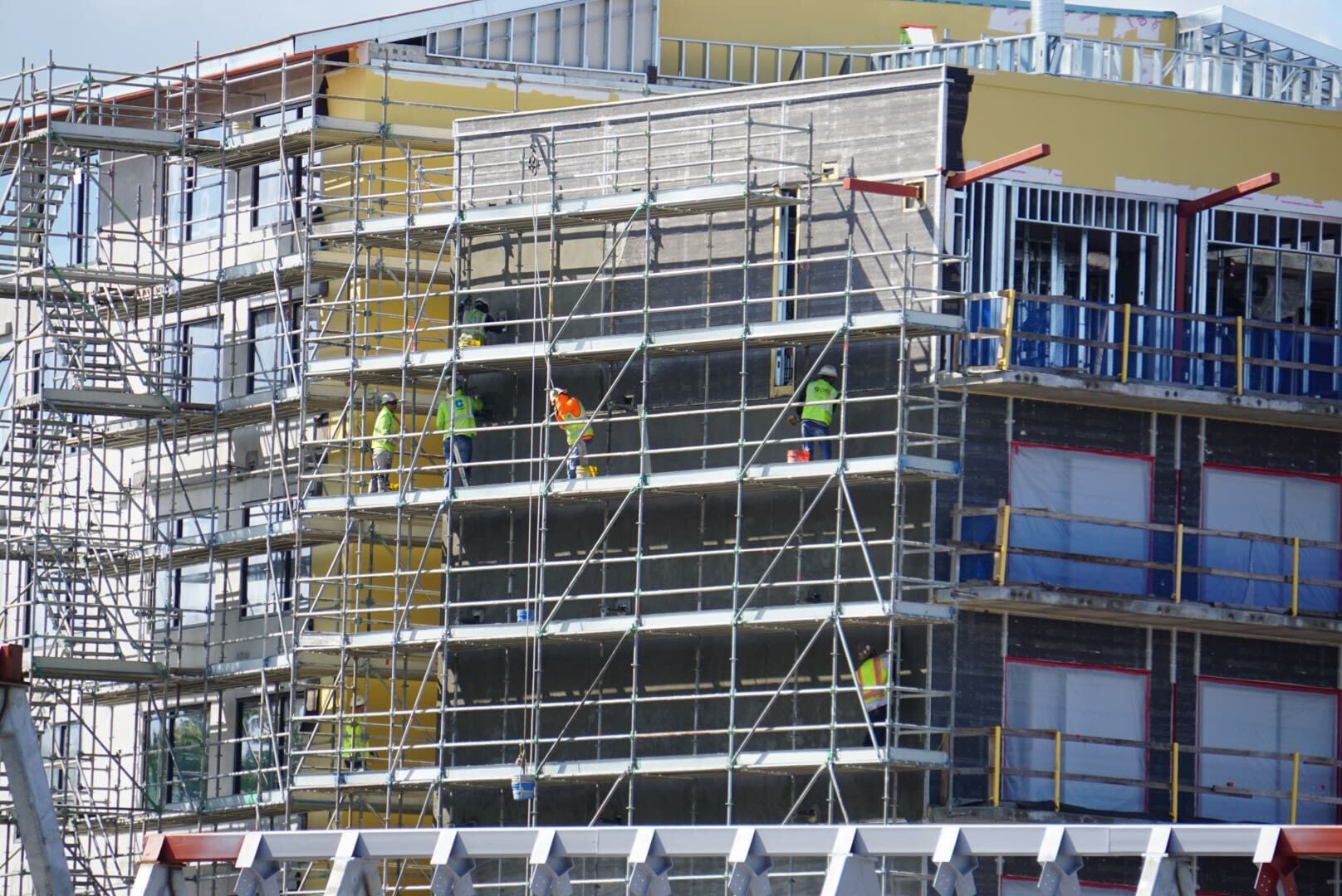 Construction workers in safety gear stand on scaffolding at Disney Lakeshore Lodge, a multi-story building under construction.