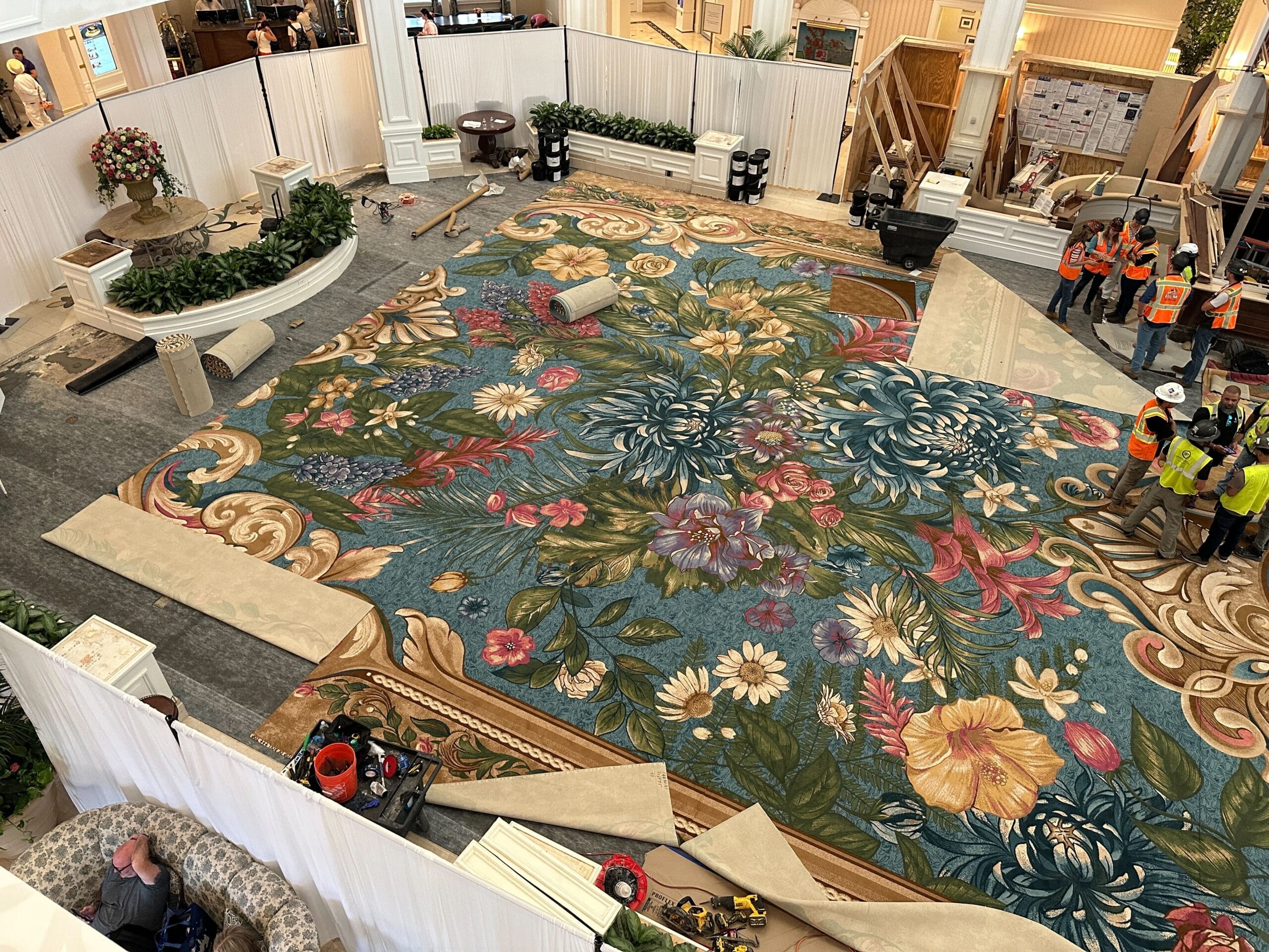 Workers in safety vests install a bright floral carpet at the Grand Floridian, its interior grand like a Disney castle lobby.