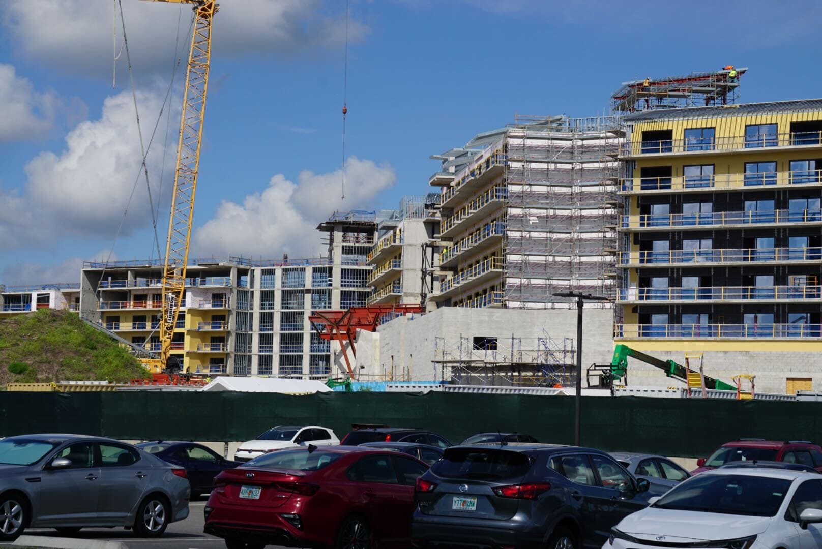 A construction site near Lakeshore Lodge with cranes, scaffolding, and partially built apartments behind a car-filled lot.