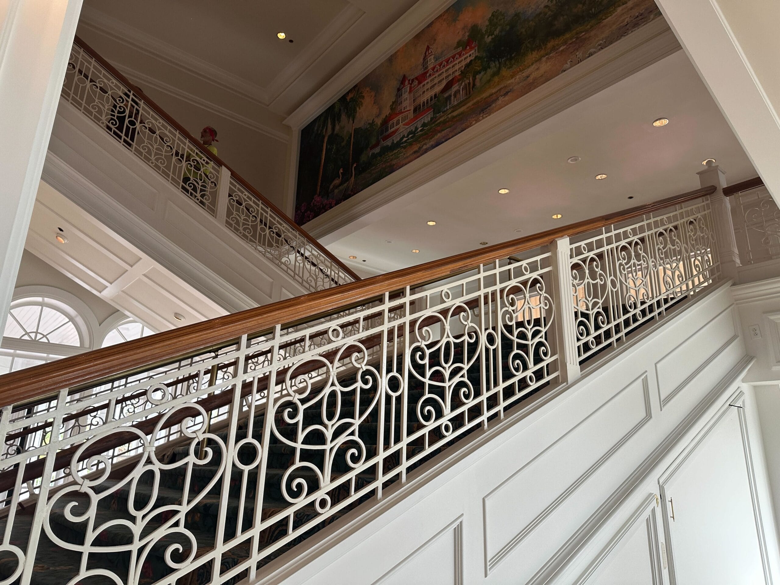 Elegant white staircase with ornate railing, leading up to a mural of a building and trees above the landing.