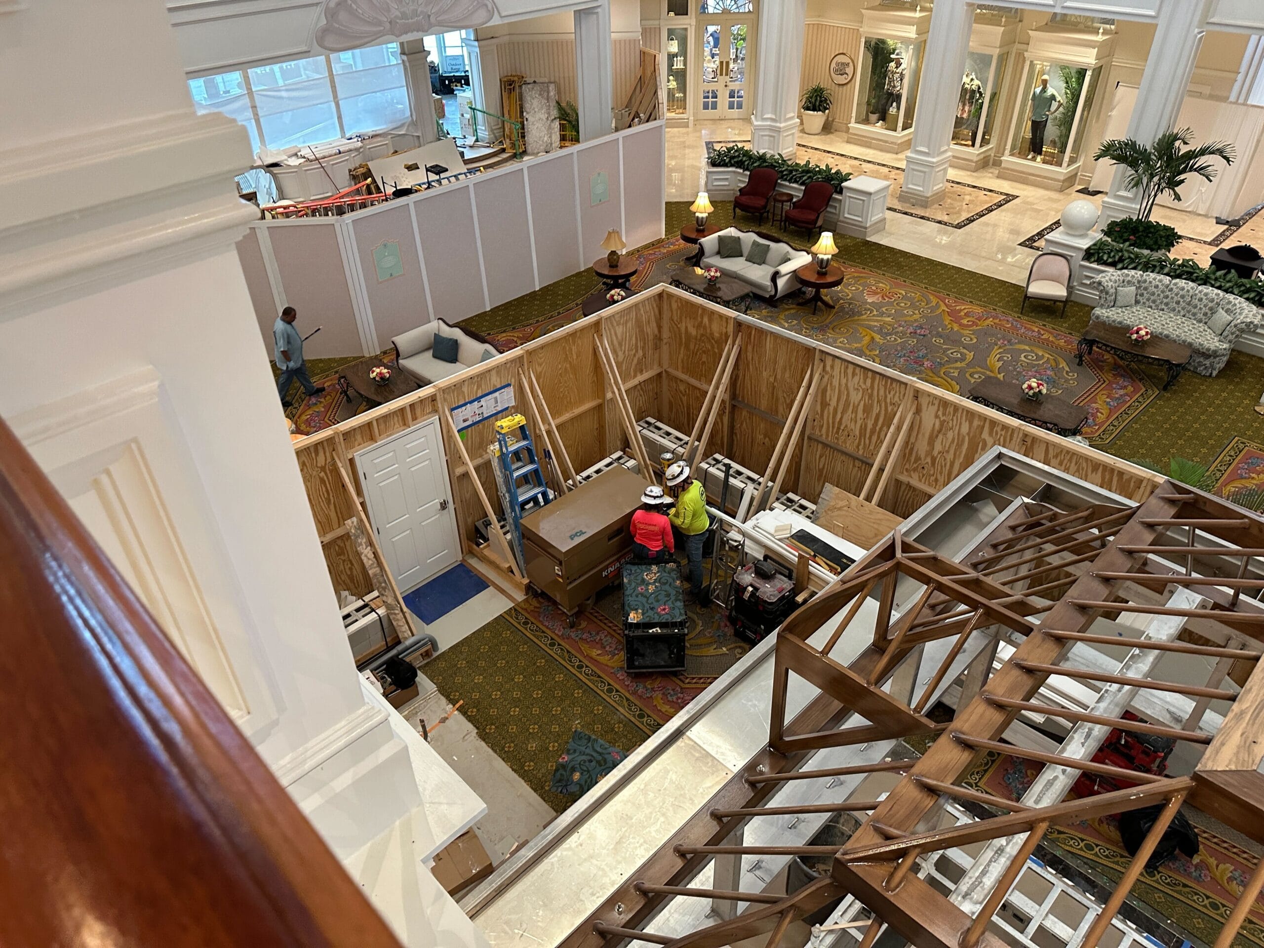 A hotel lobby under renovation with workers, wooden barriers, tools, and furniture scattered around.