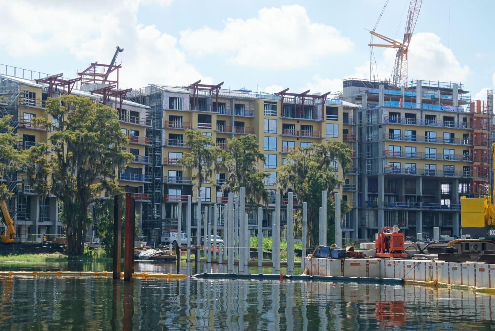 Modern apartment complex under construction by the waterfront, near Lakeshore Lodge, with cranes and equipment visible.