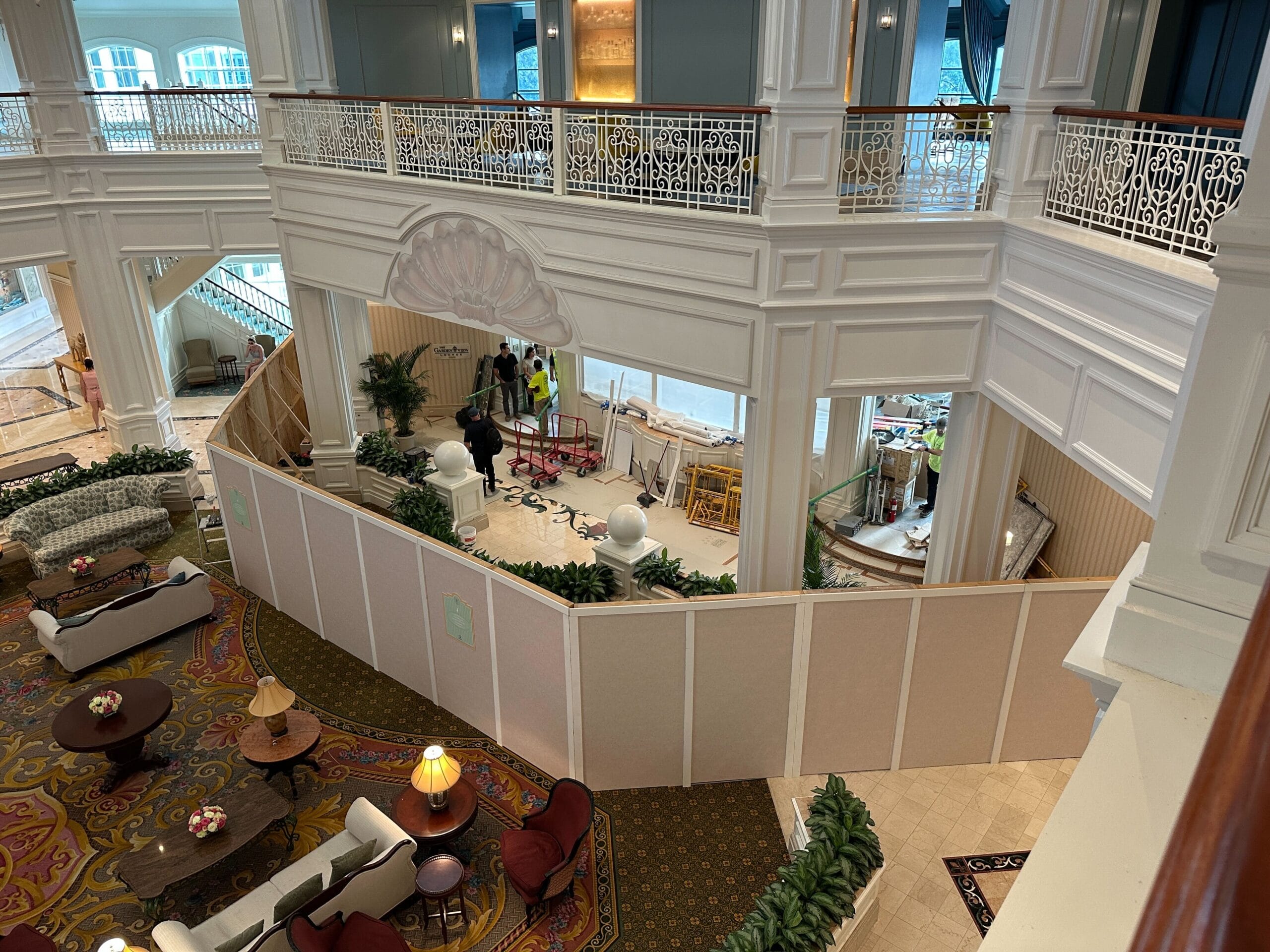 A hotel lobby with Grand Floridian construction walls enclosing the Tea Room, and workers visible behind the barrier.