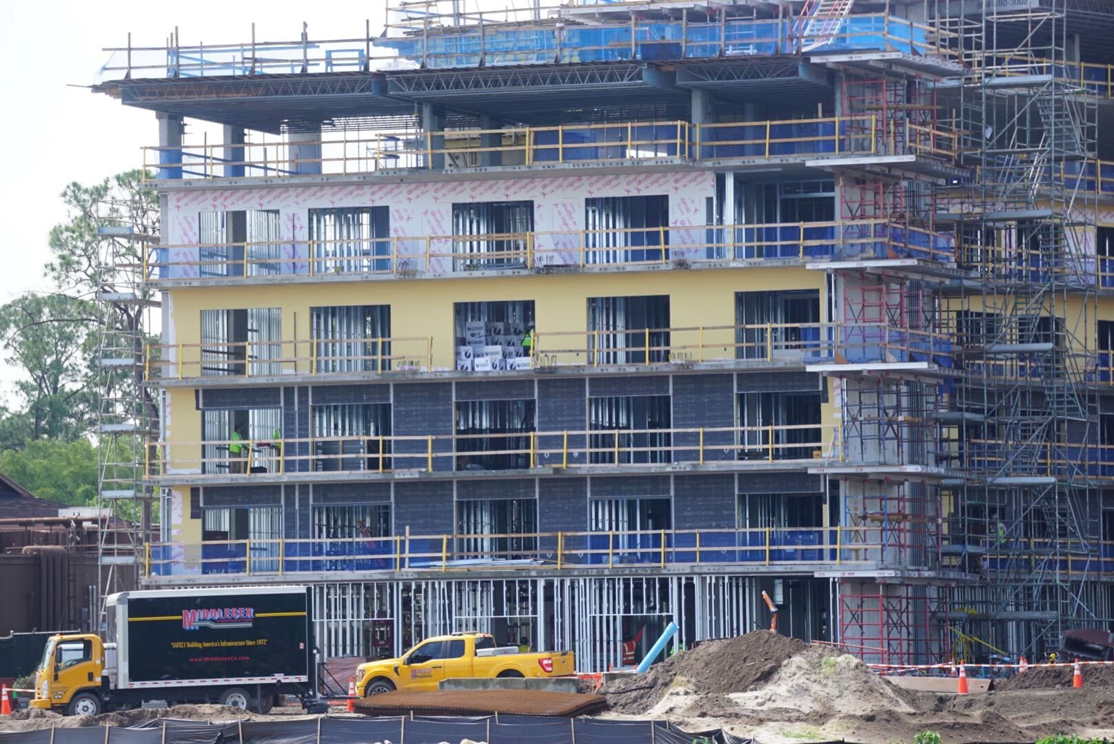 A multi-story building under construction with scaffolding, vehicles, and construction materials in the foreground.