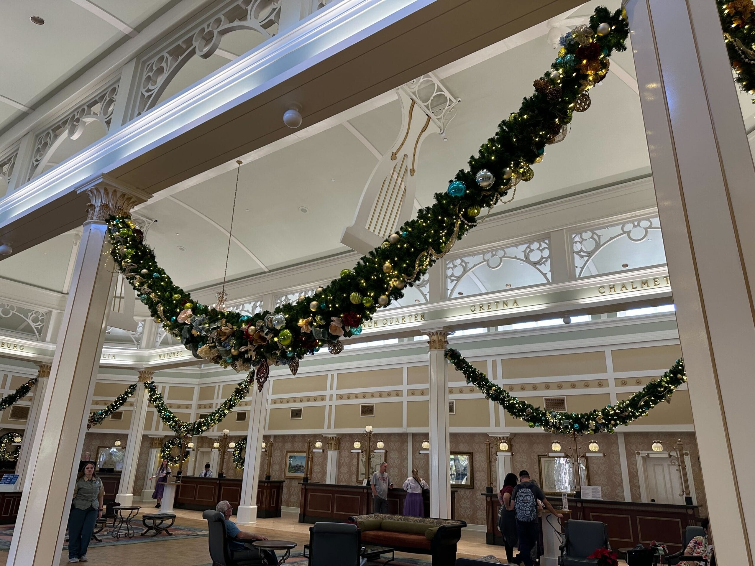 Ornate lobby with high ceilings, decorated with festive garlands and glowing lights. People are seated and standing near a reception desk.