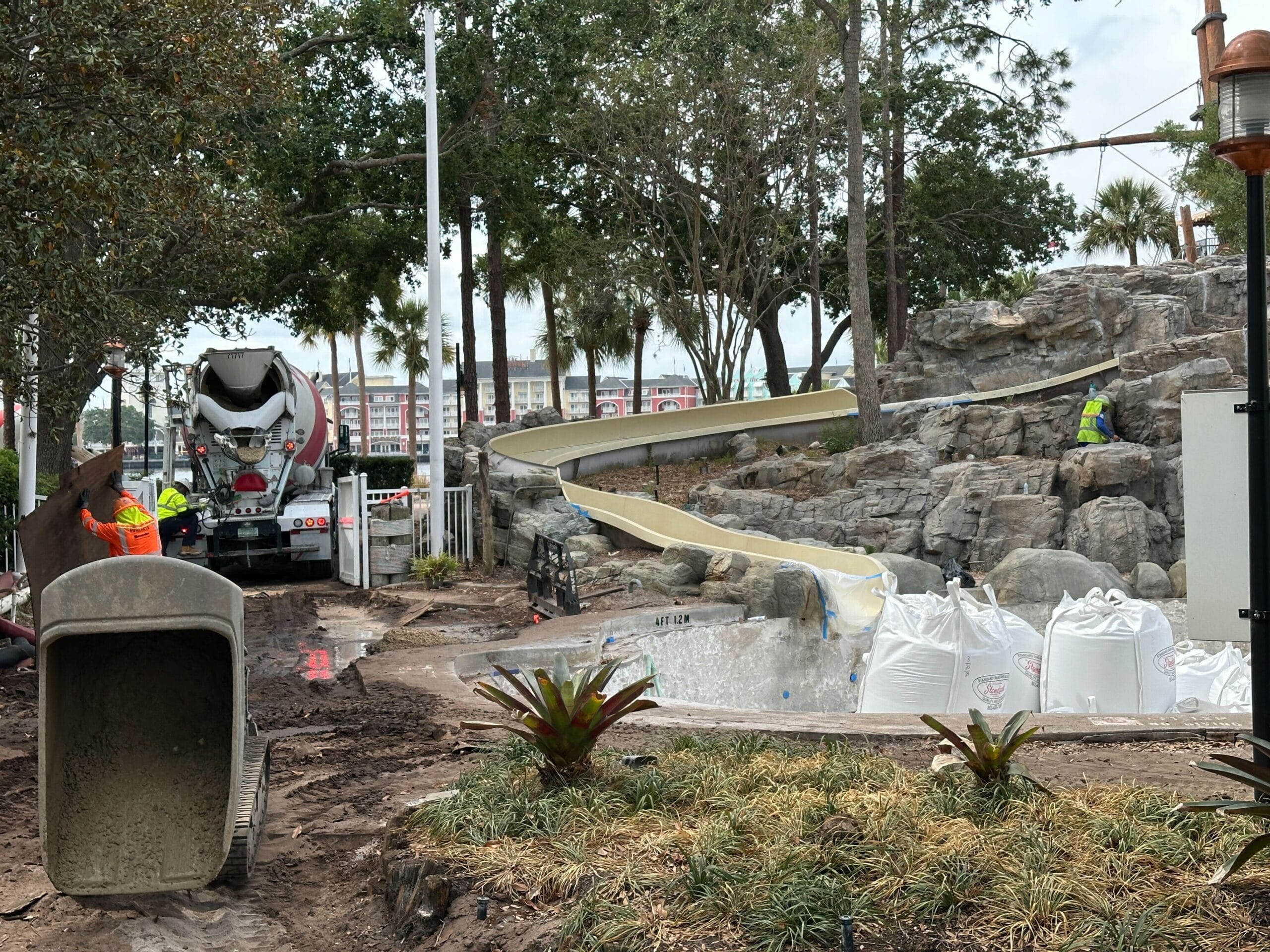 Construction workers building a waterslide with rocks, plants, and a cement truck at a work site.