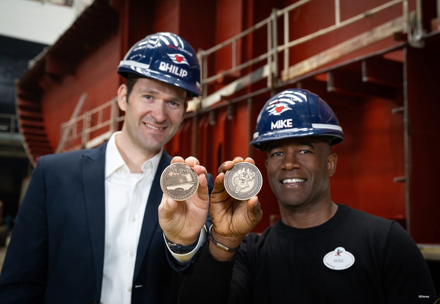 two people with helmets in front of a disney cruise ship holding disney destiny cruise and minnie mouse keel coins