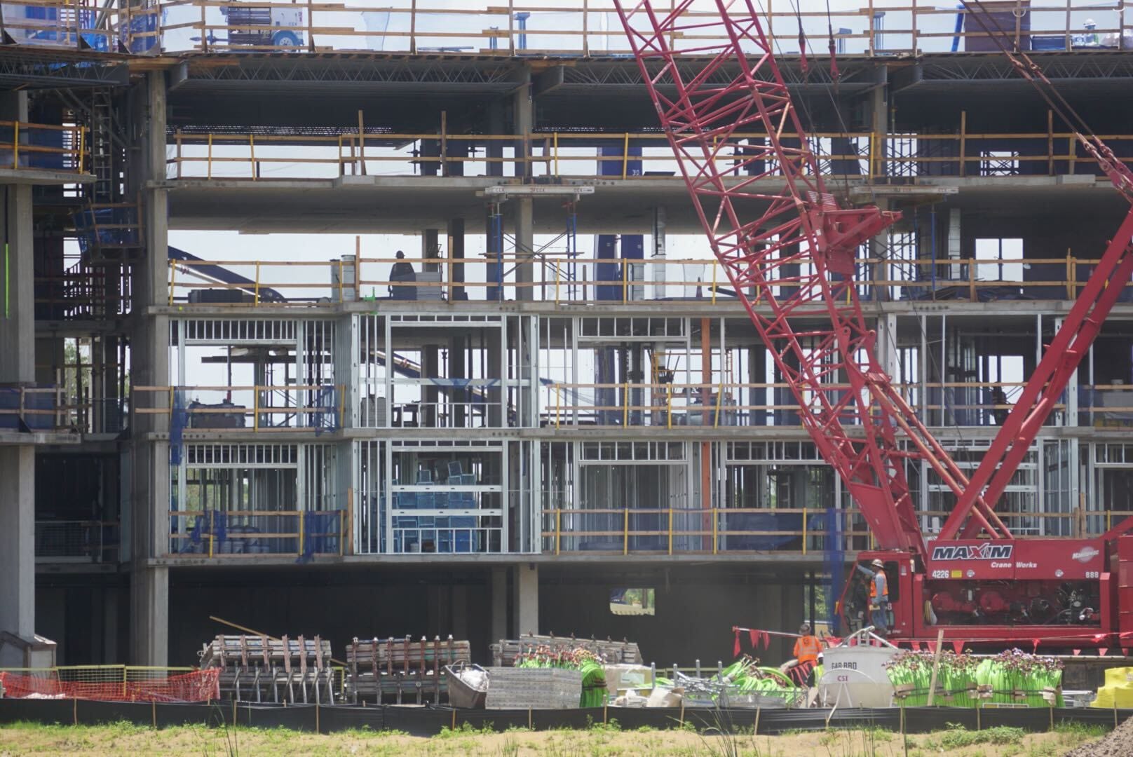 A multi-story Disney hotel under construction with workers, scaffolding, and a large red crane in front.