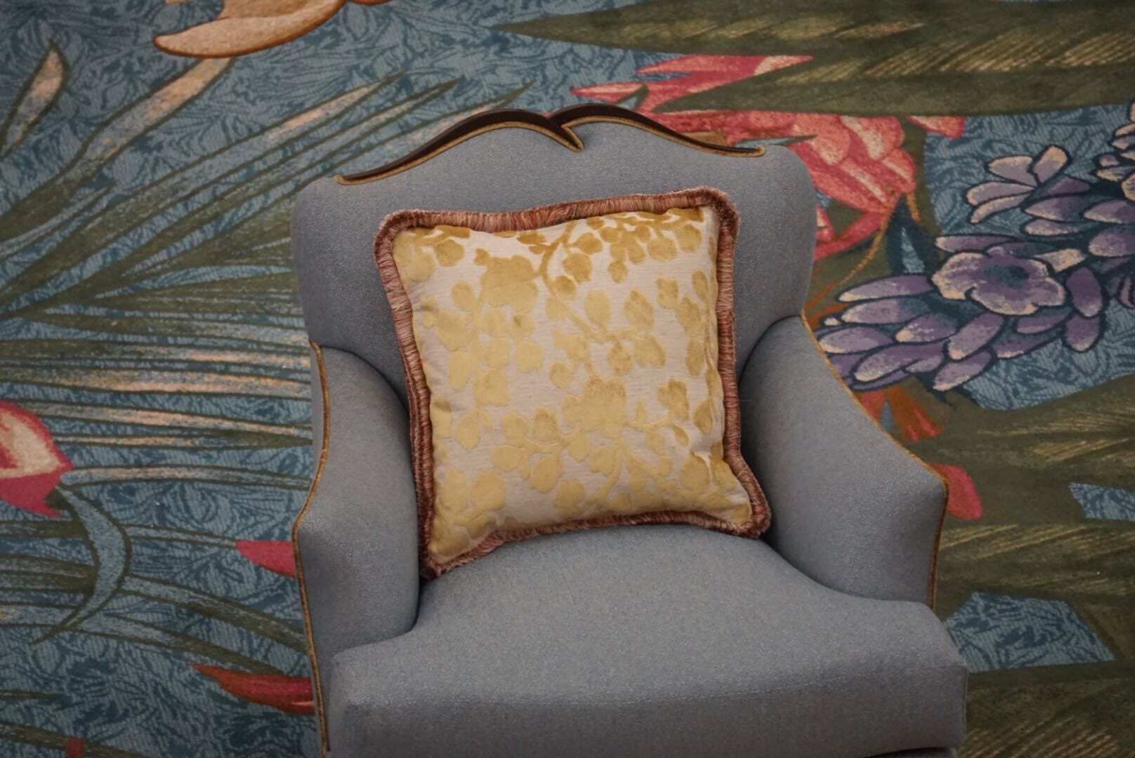 Blue armchair with yellow floral cushion, Grand Floridian Resort lobby style, sits on floral carpet reminiscent of Disney park elegance.