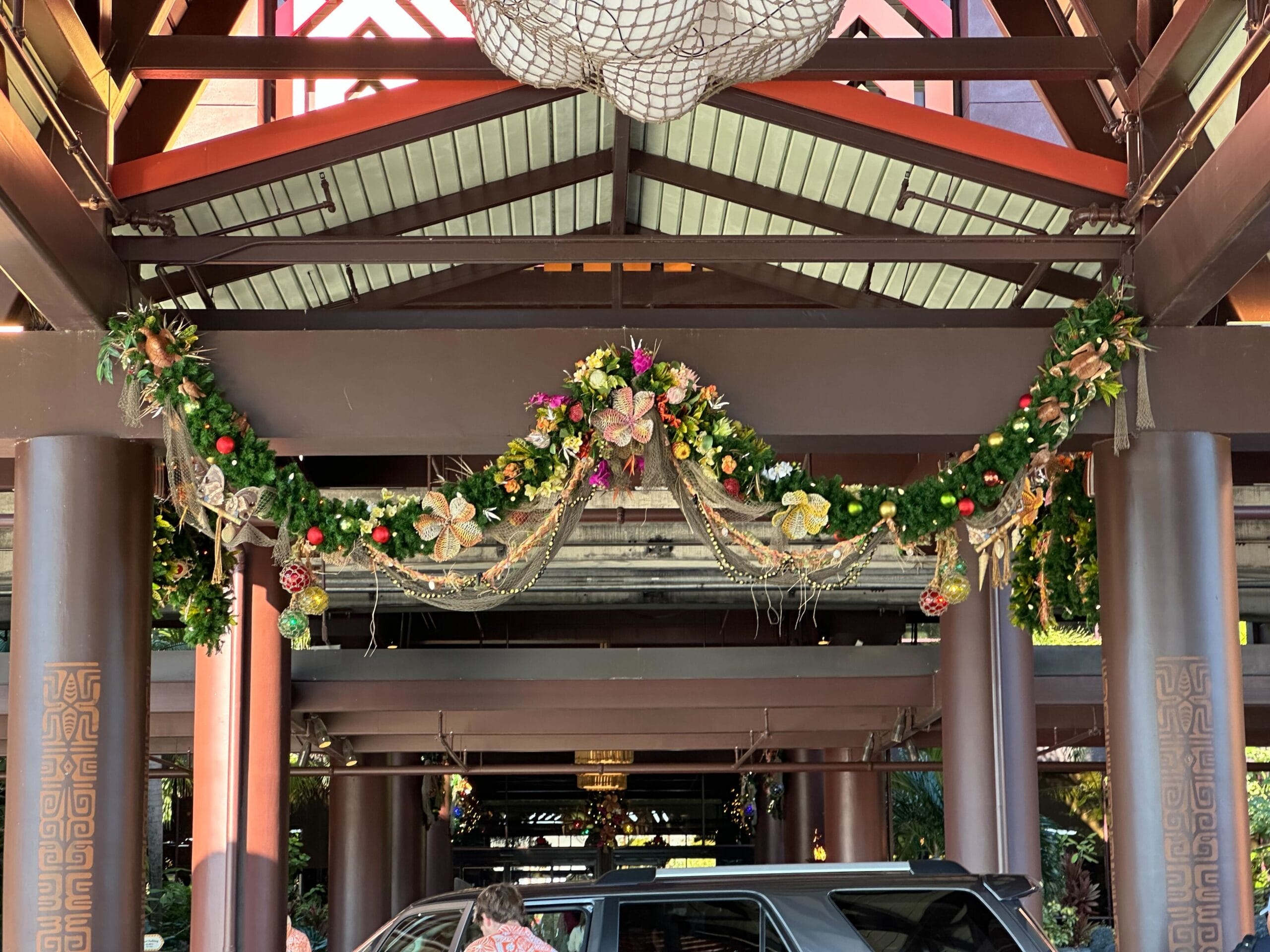 A car is parked under a decorated structure with festive garlands and ornaments hanging from the ceiling.