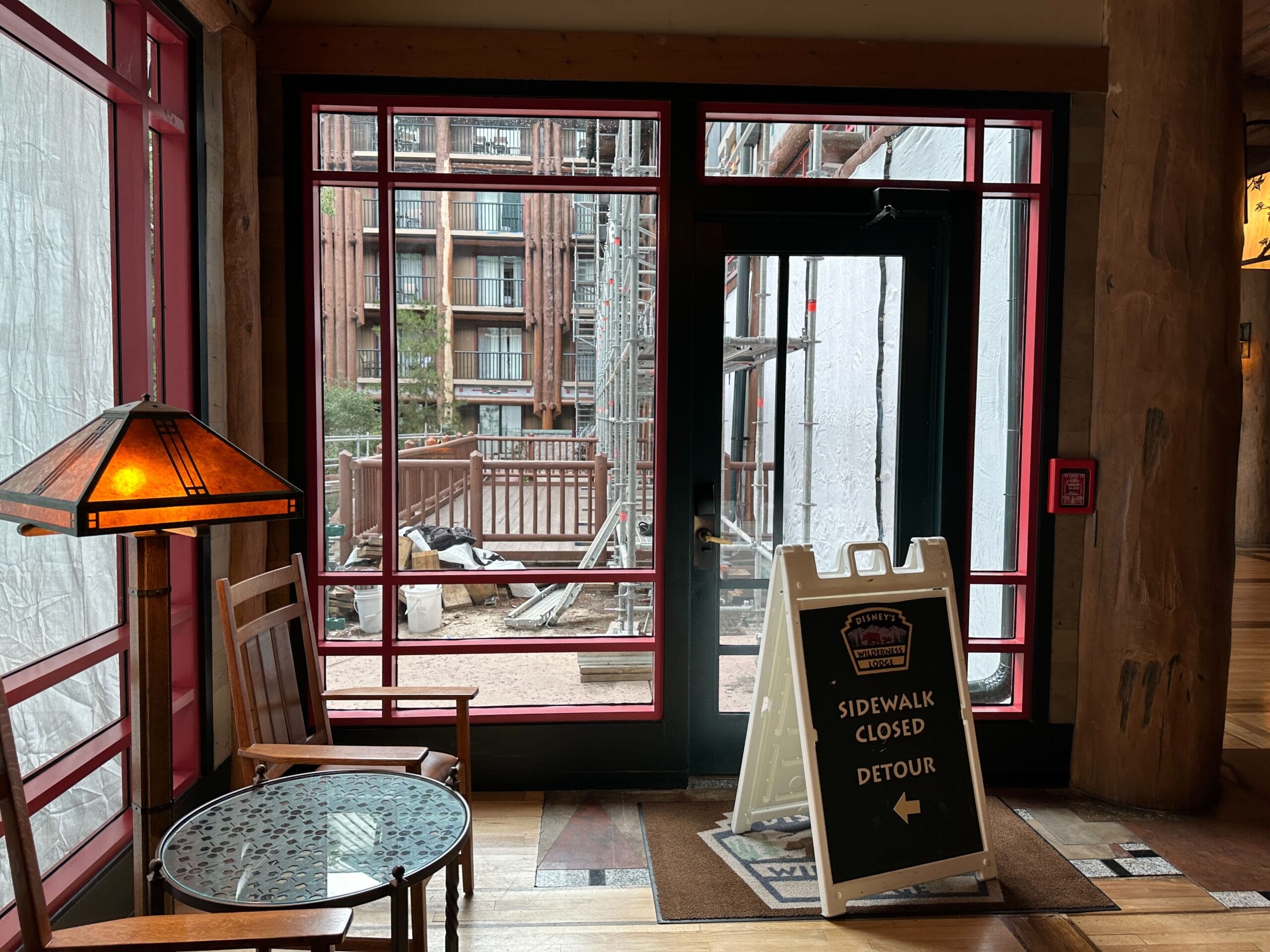 Indoor area with table and chairs; outside, a Sidewalk Closed Detour sign hints at a Wilderness Lodge update nearby.