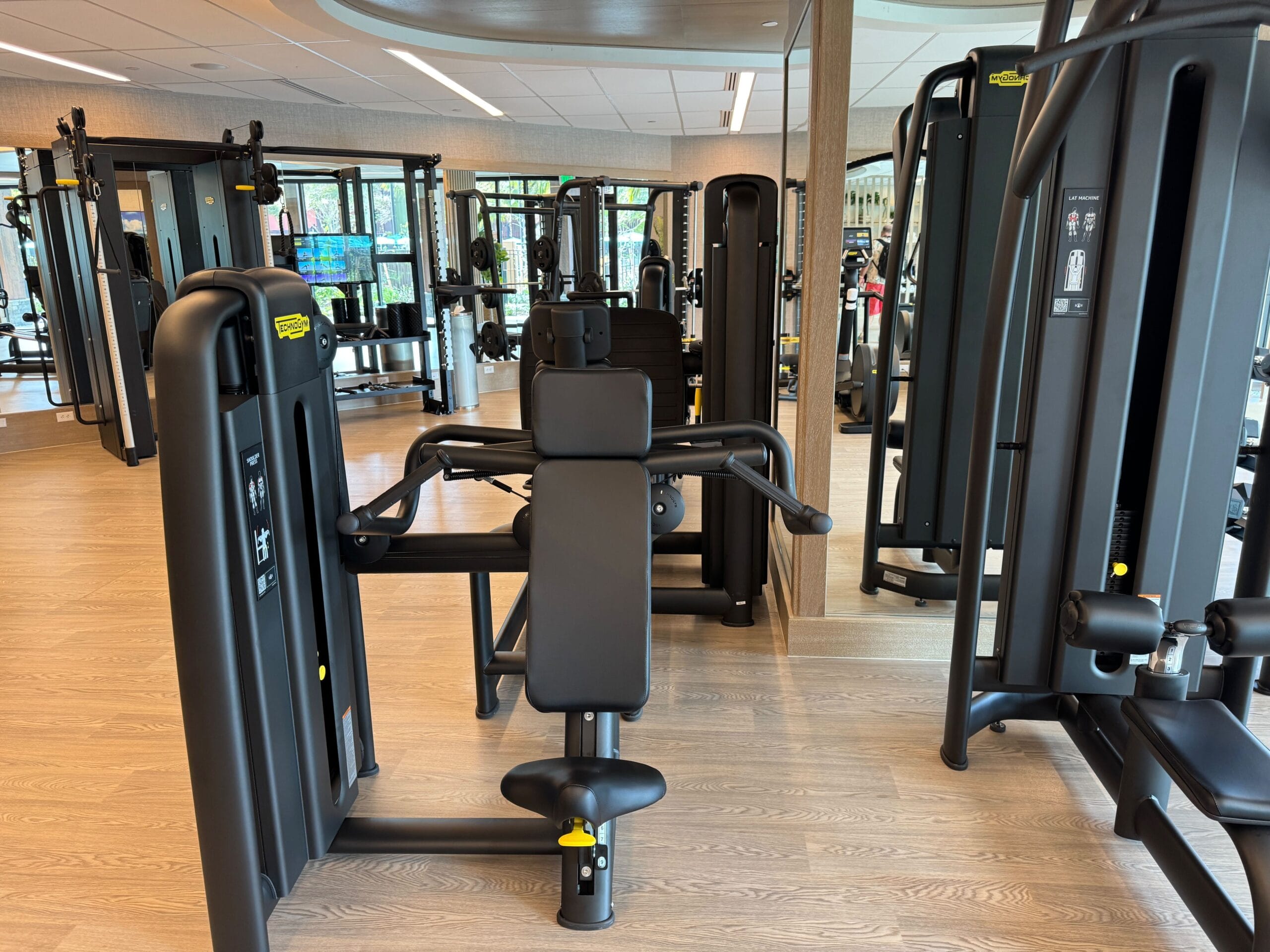 A gym room featuring various exercise machines, including weightlifting equipment and mirrors on the walls.
