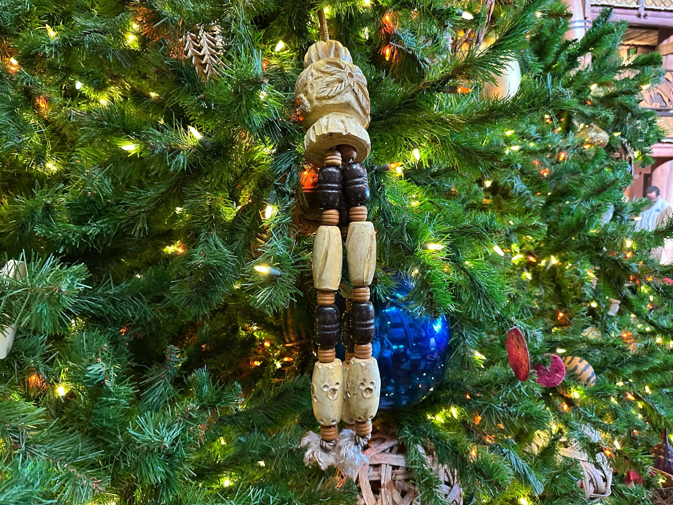 Wooden beaded ornament hanging on a decorated Christmas tree with lights.