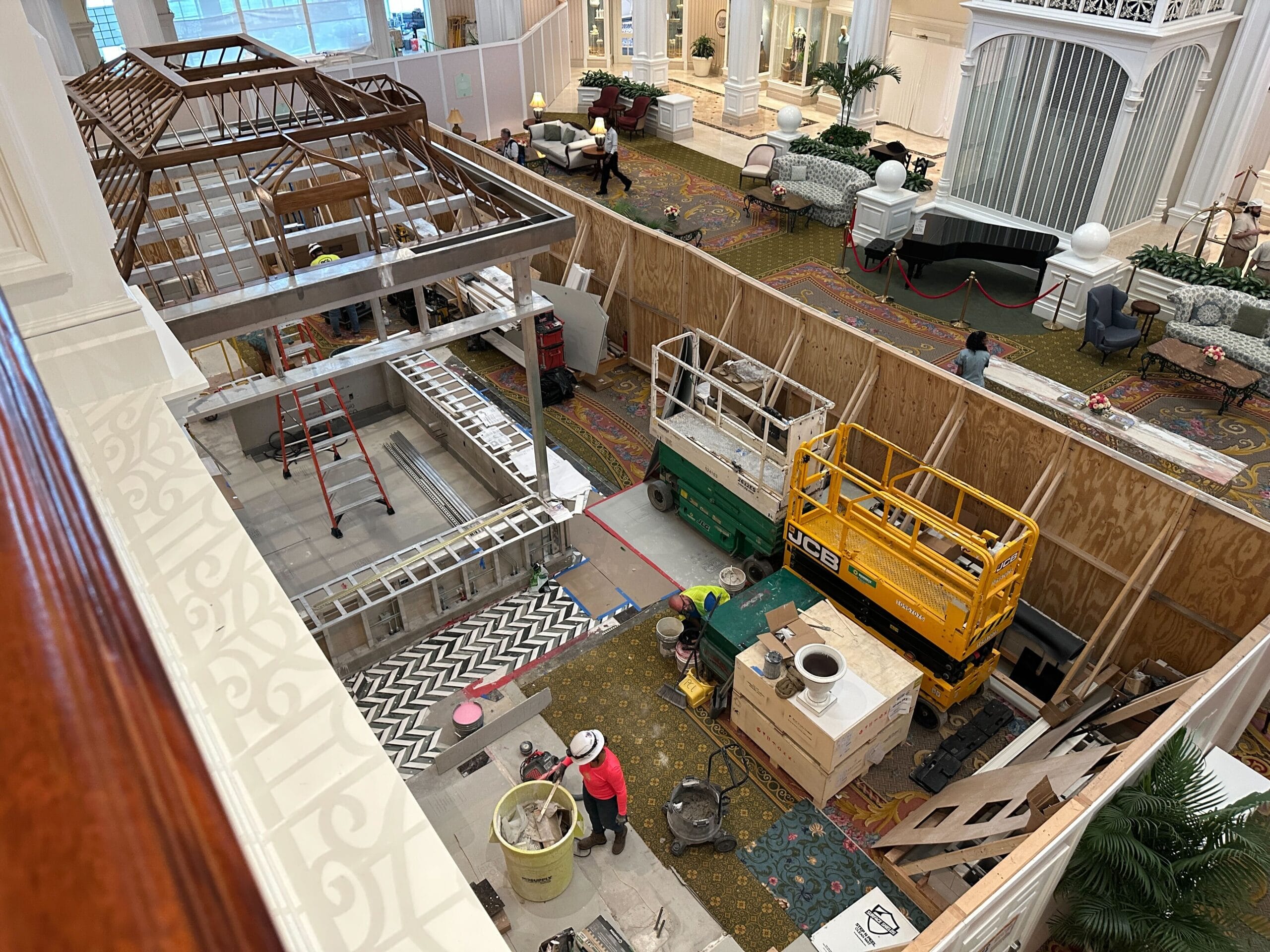 Hotel lobby under construction with workers, equipment, and wooden barriers surrounding the renovation area.