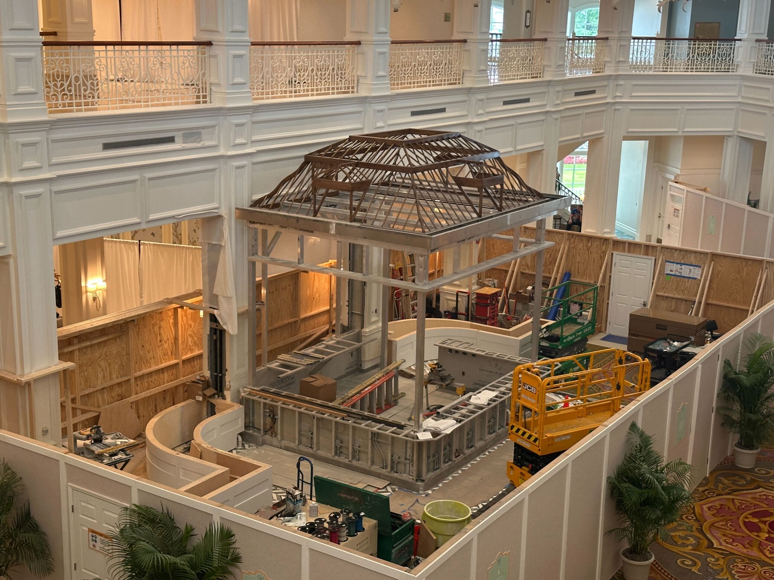 Construction site inside a large building with scaffolding, equipment, and an unfinished dome structure overhead.
