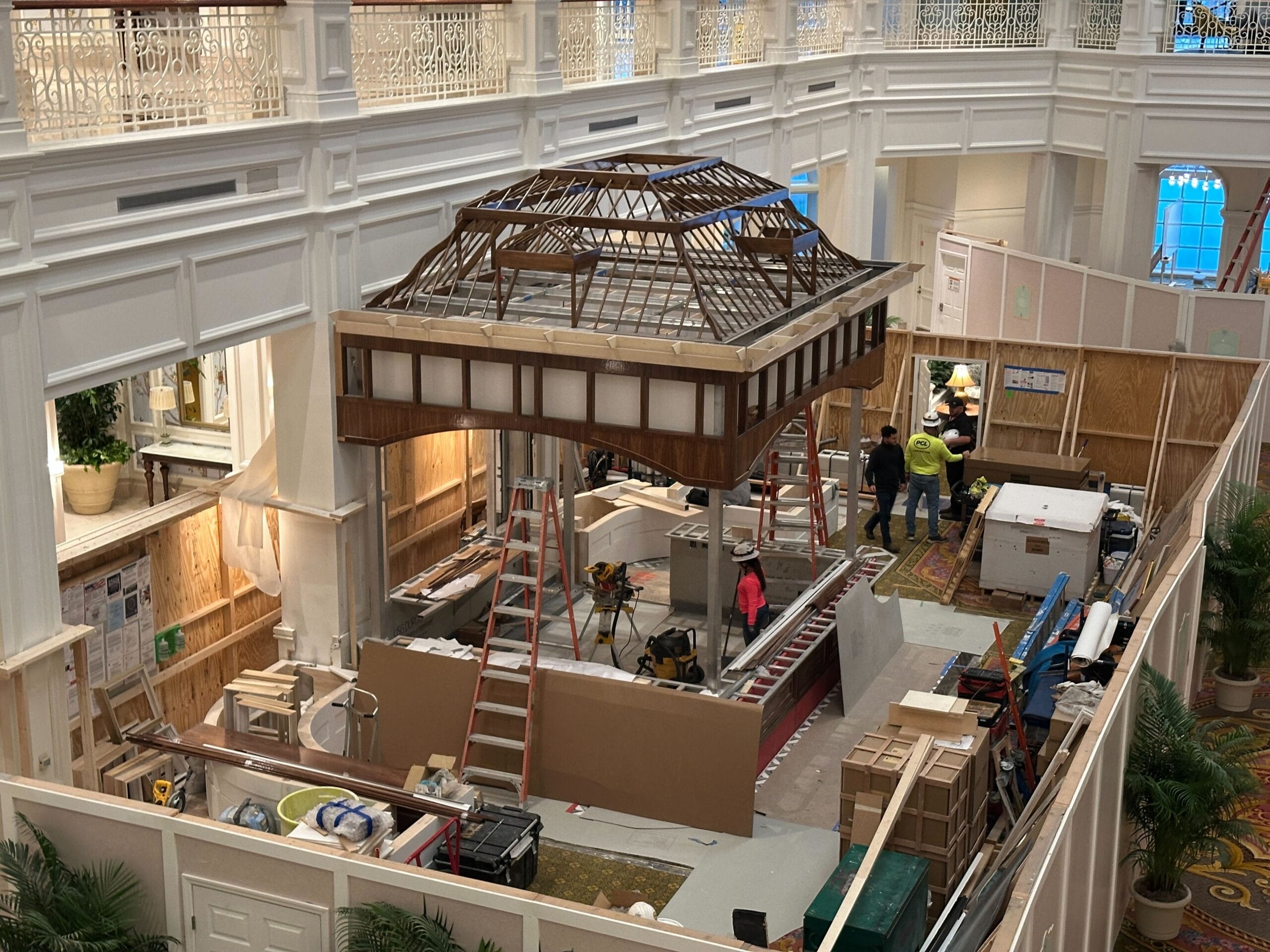 A partially constructed wooden gazebo at the Grand Floridian is surrounded by workers and building materials indoors.