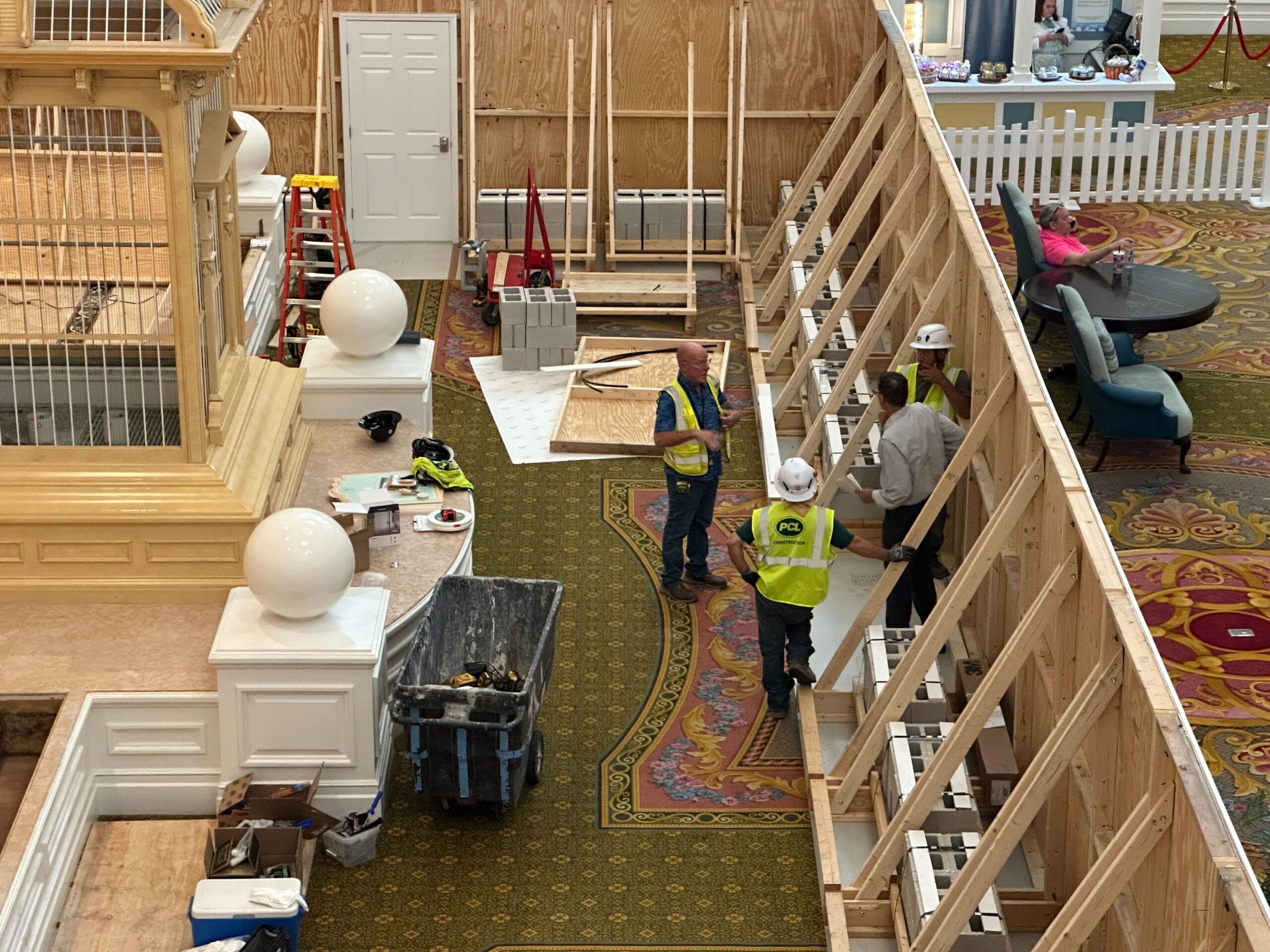 Four workers in safety vests examine lobby construction near a wooden wall at the Grand Floridian.