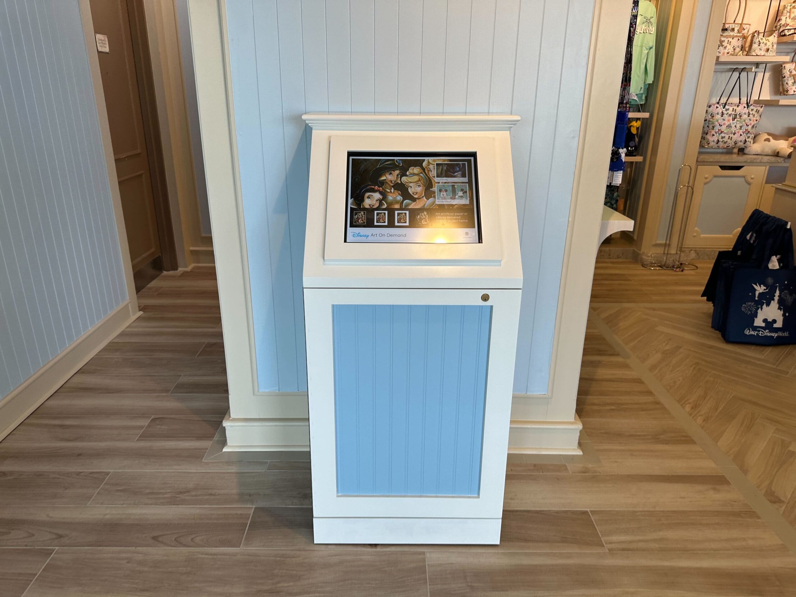 A display kiosk featuring Disney animated characters dances on the screen, enclosed in a sleek white and blue frame. Positioned on the wooden floors of a retail store, it's reminiscent of the charming Boardwalk Inn Resort ambiance, with shelves full of enticing merchandise in the backdrop.