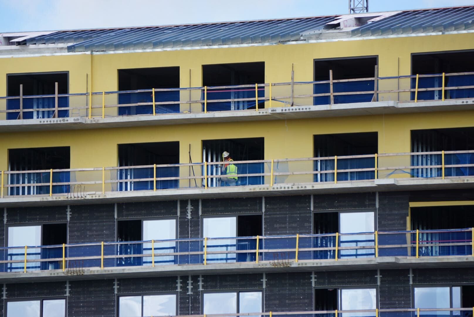 A construction worker in a yellow vest stands on the balcony of a building under construction.