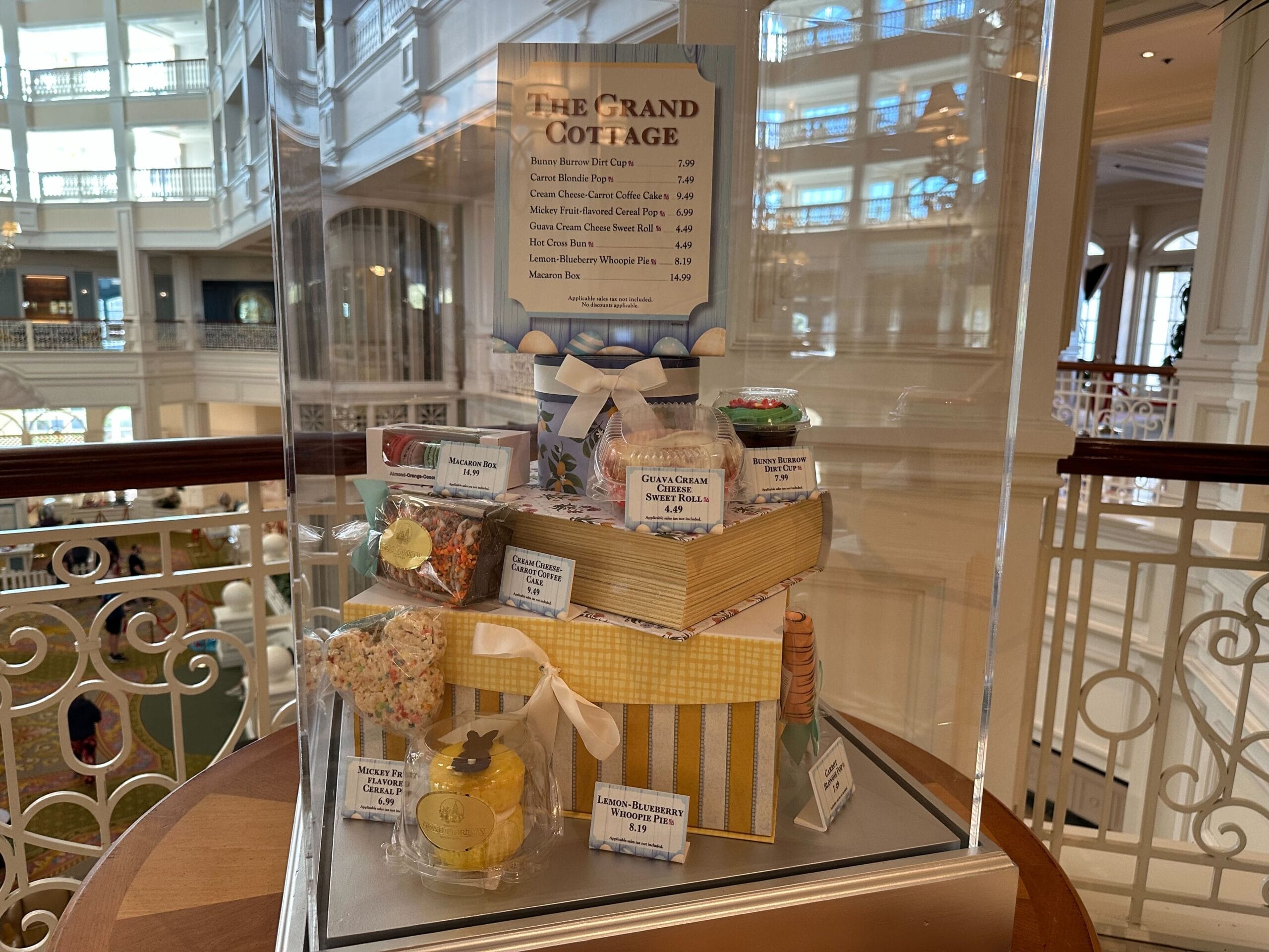 A display case features various confectioneries, including cookies and chocolates, adorned with bows and ribbons. A price list for the items is visible at the top.