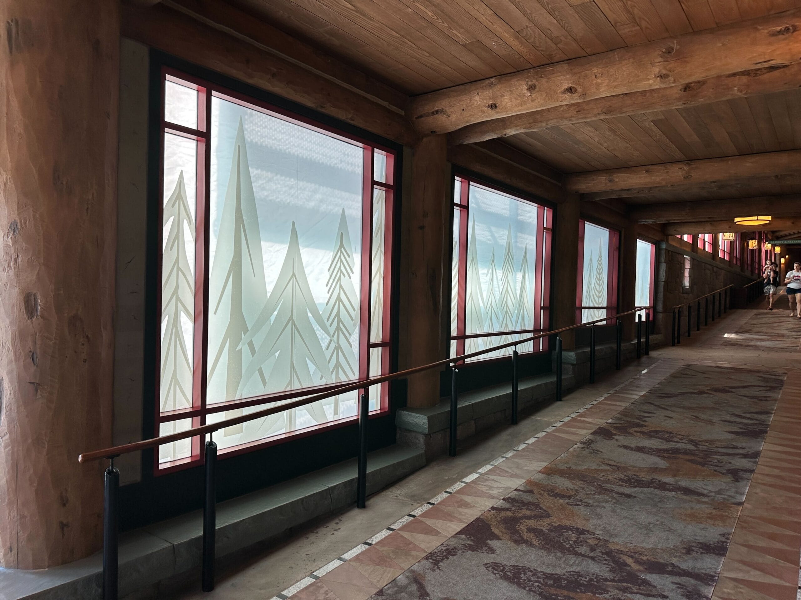 A resort-style hallway at Fort Wilderness Lodge with wood beams and frosted windows etched with tree designs.