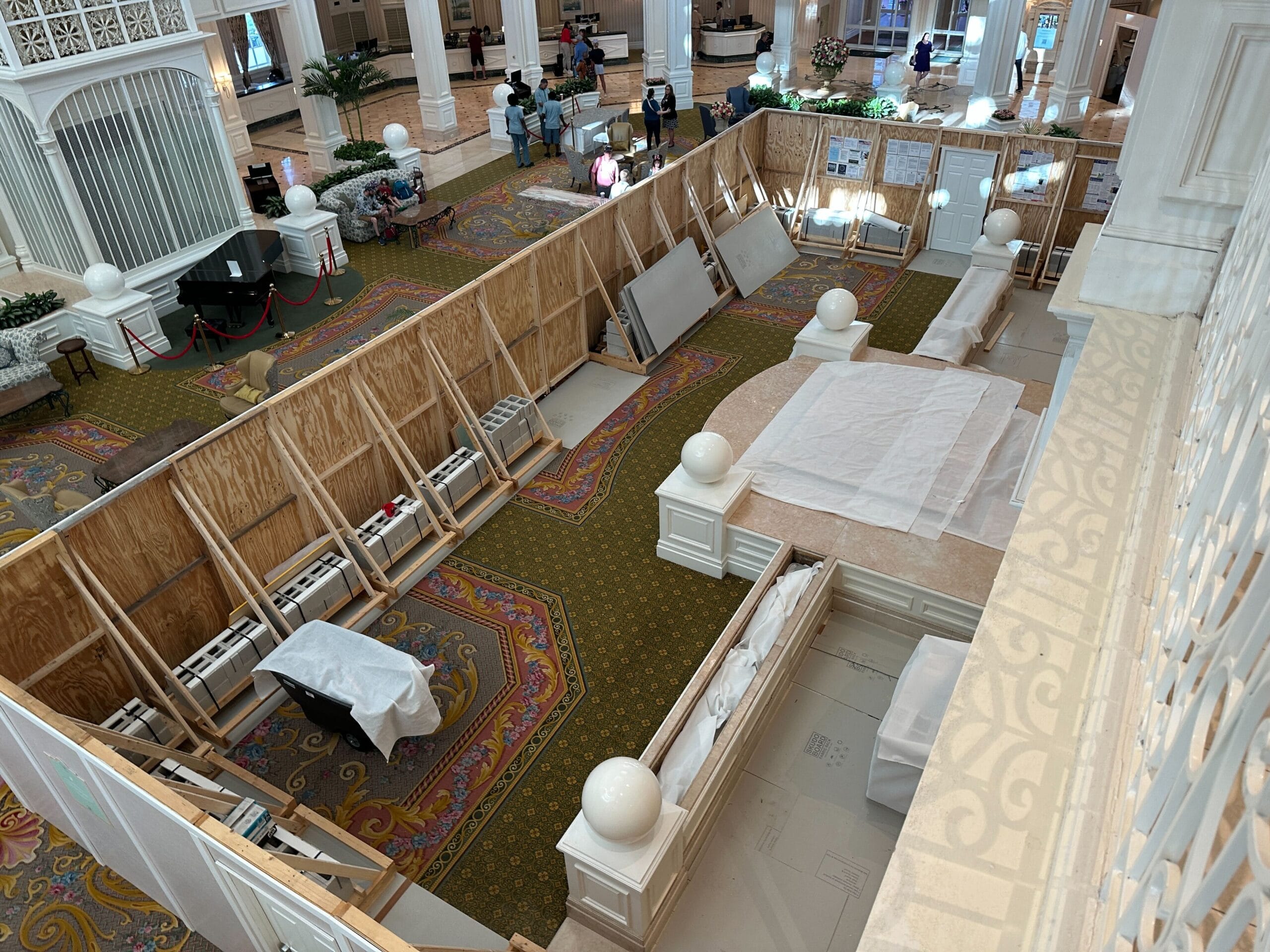 Hotel lobby at Grand Floridian Resort under renovation, with wooden barriers, covered furniture, and Disney-themed birdcage visible.
