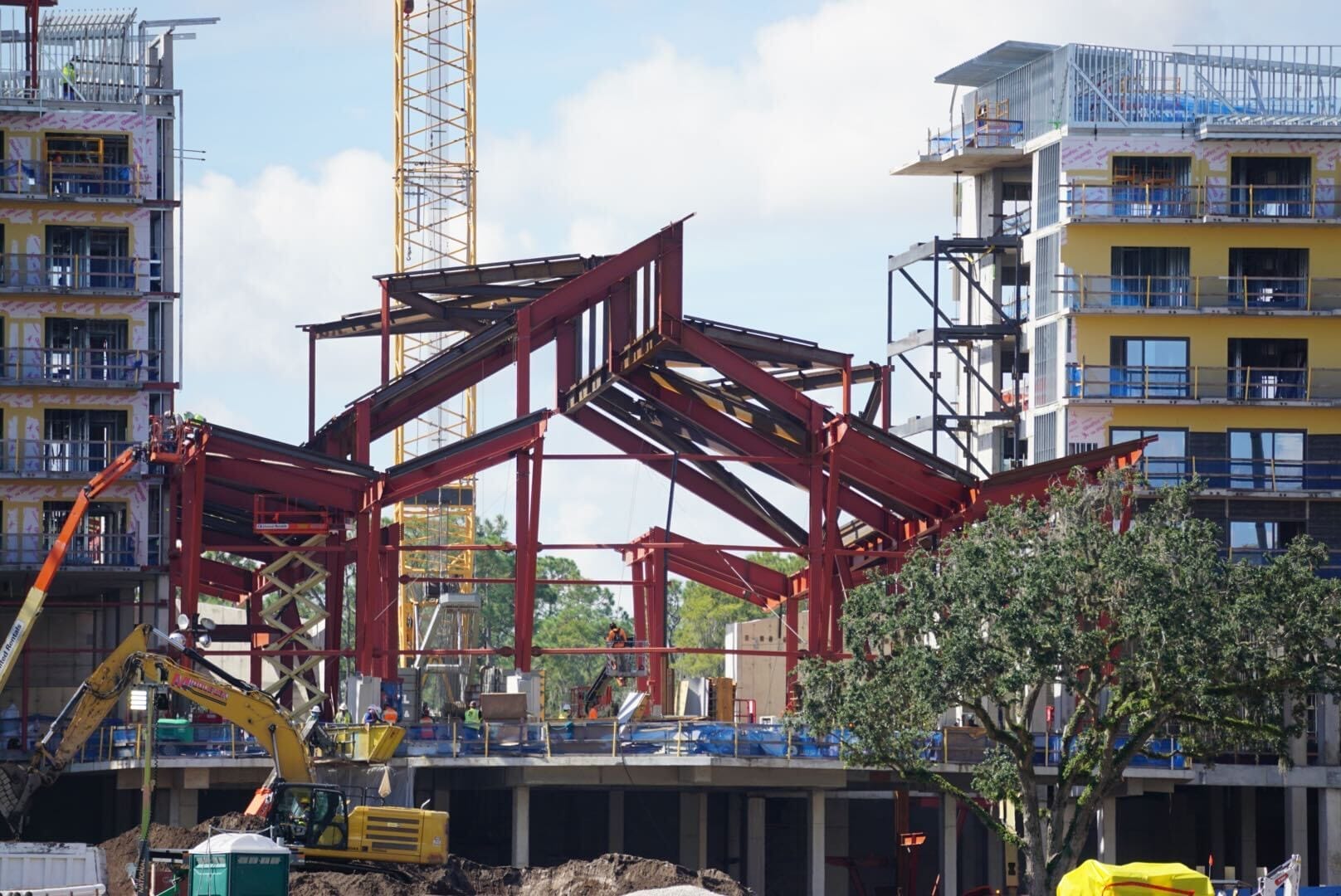 Red steel beams rise at Disney Lakeshore Lodge, with cranes and machinery busy on the construction site.
