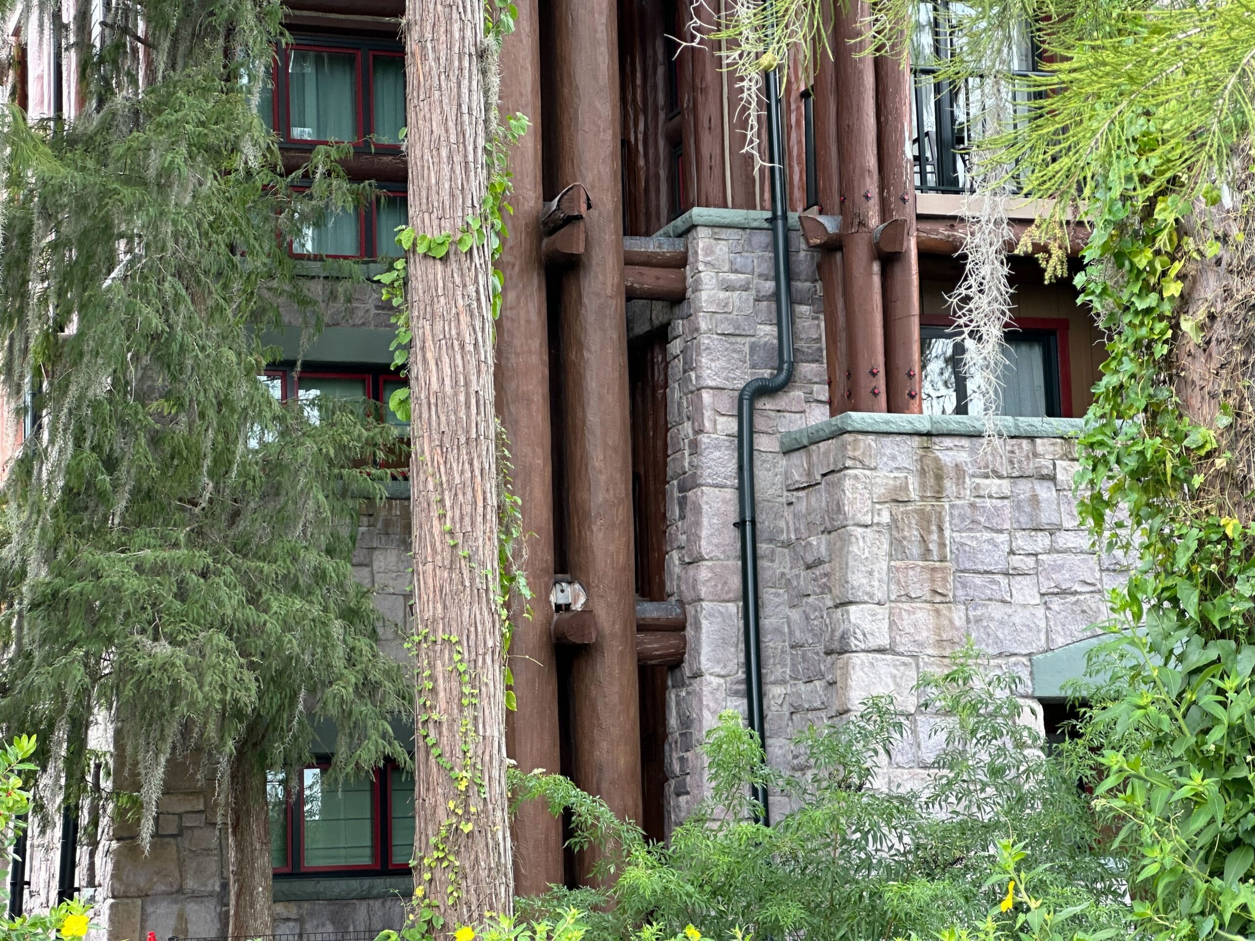 Rustic Wilderness Lodge exterior with stone walls, large wooden beams, and lush surrounding greenery and trees.