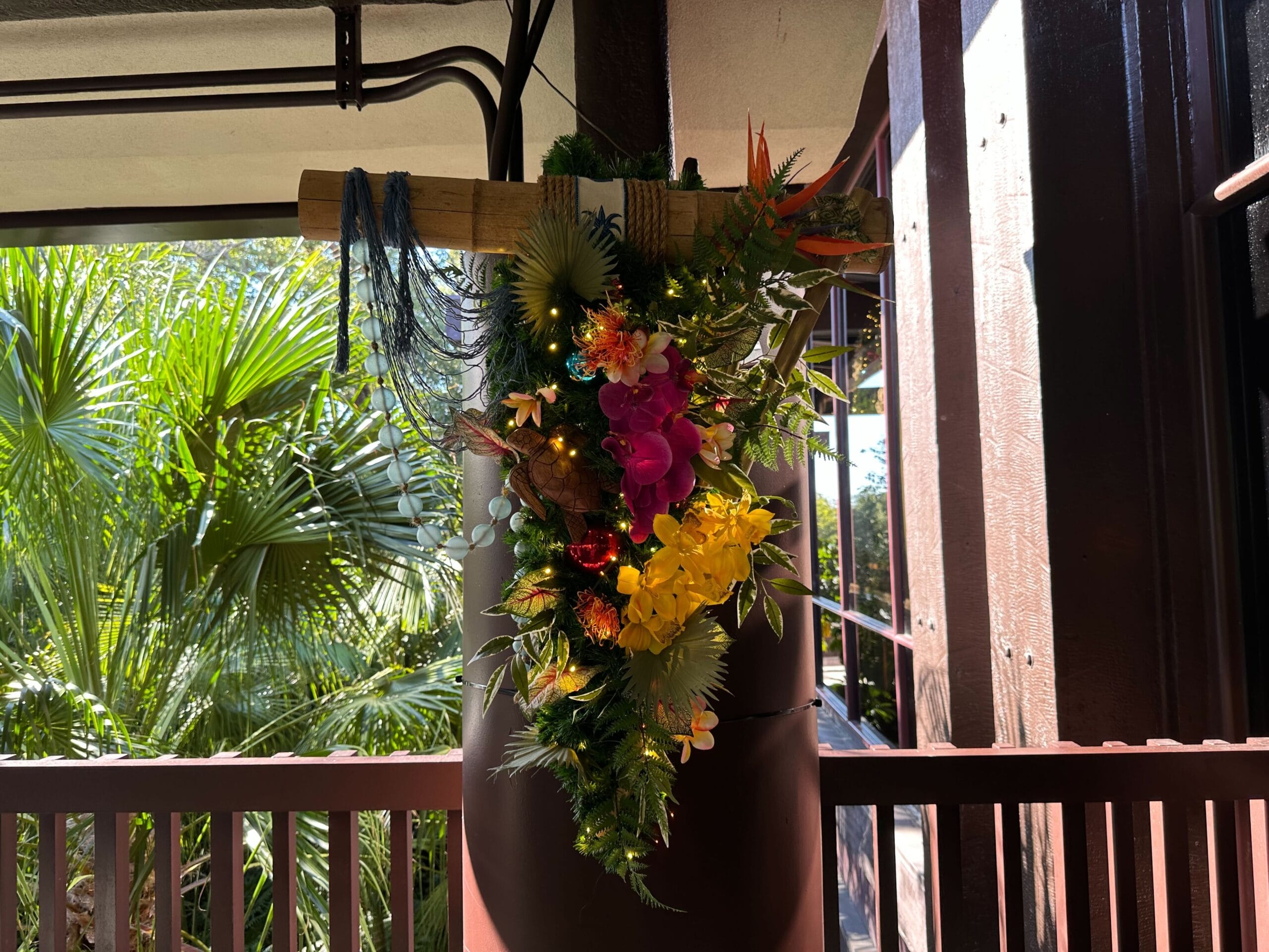 Colorful floral arrangement with tropical flowers and greenery hanging on a wooden beam in a sunlit area.