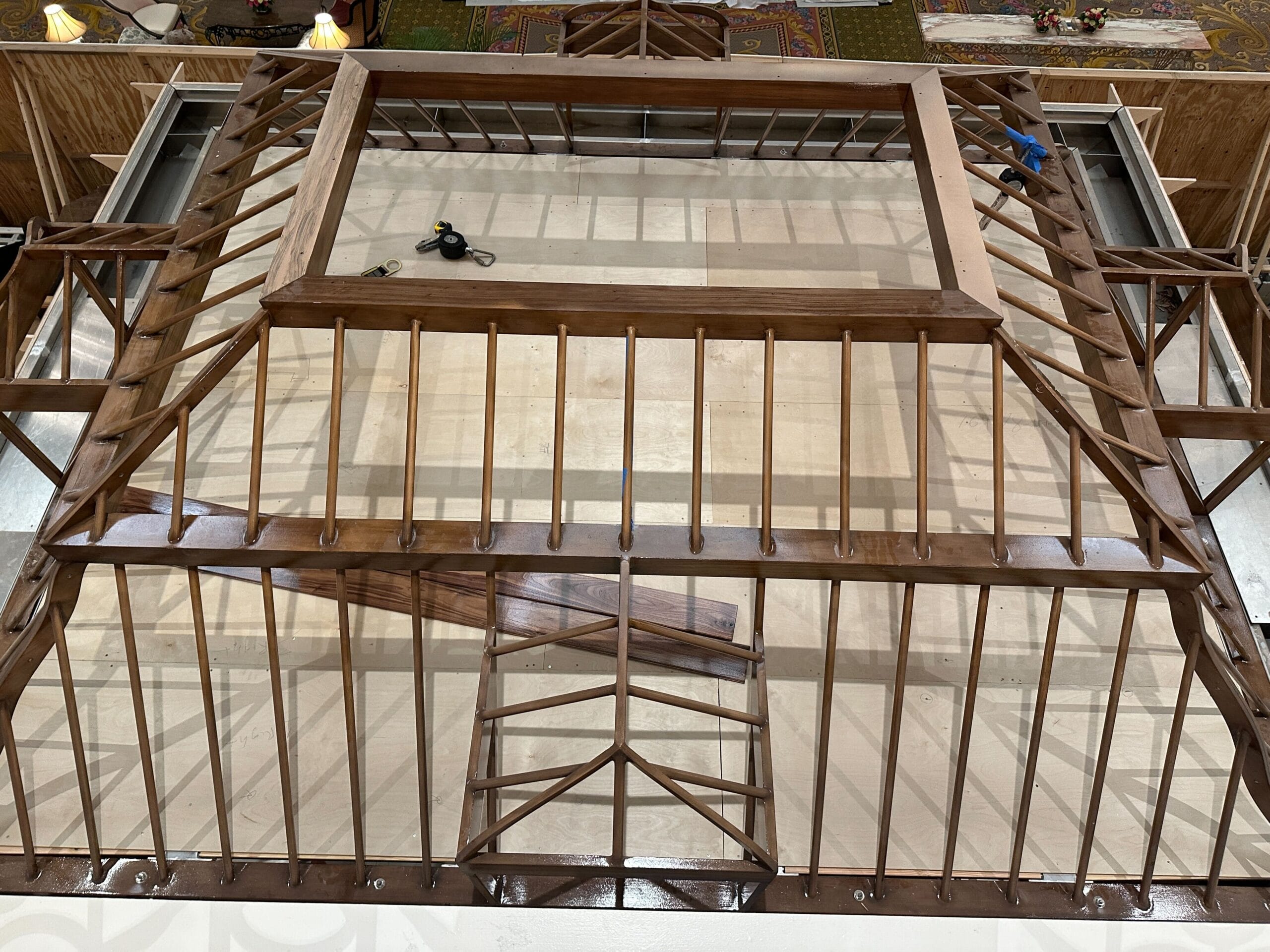 A wooden roof frame under construction, viewed from above, with beams and tools on top of a light-colored surface.