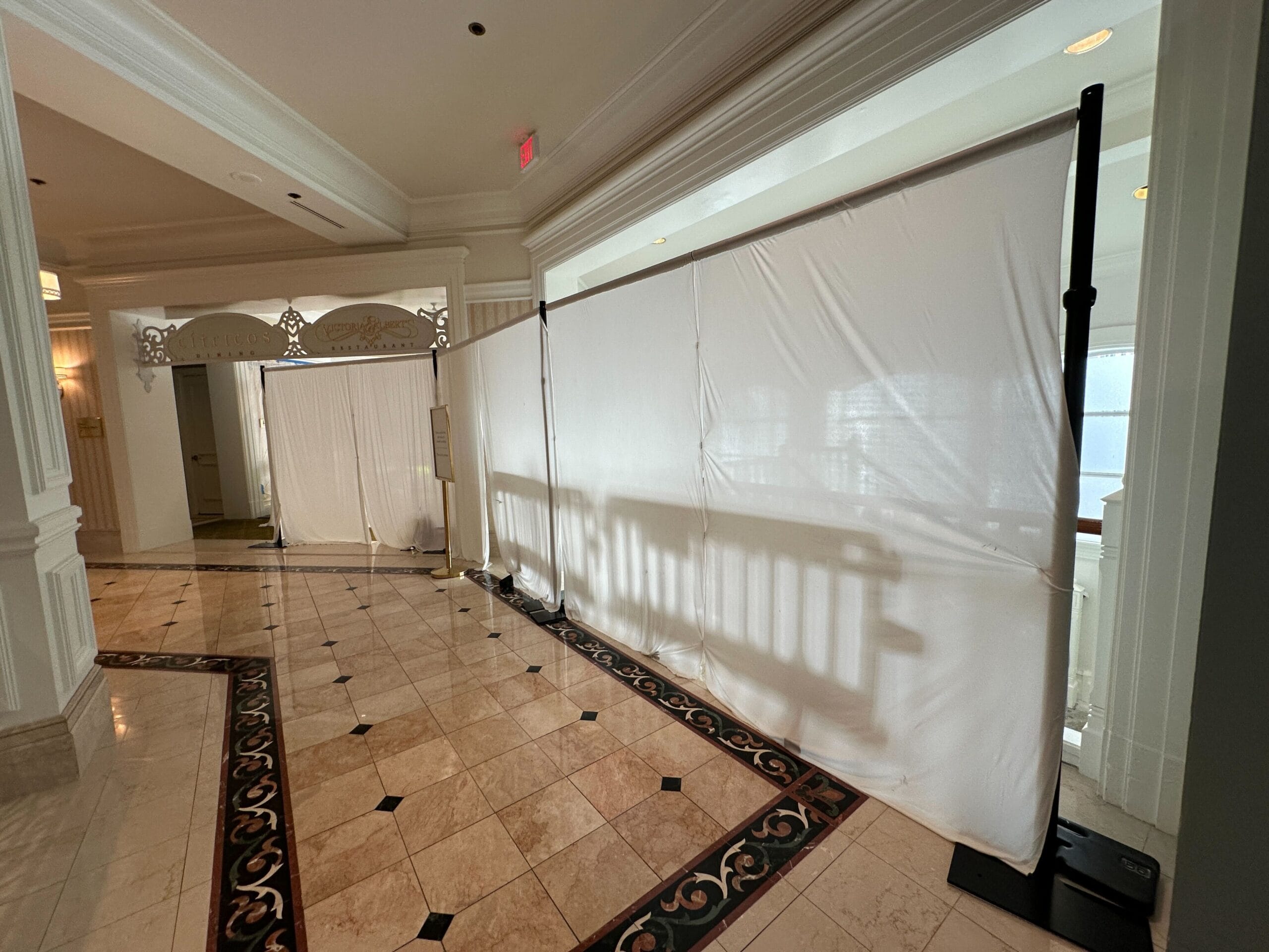 White curtains block off a hallway and entrance in a hotel with tiled floors and ornate trim.
