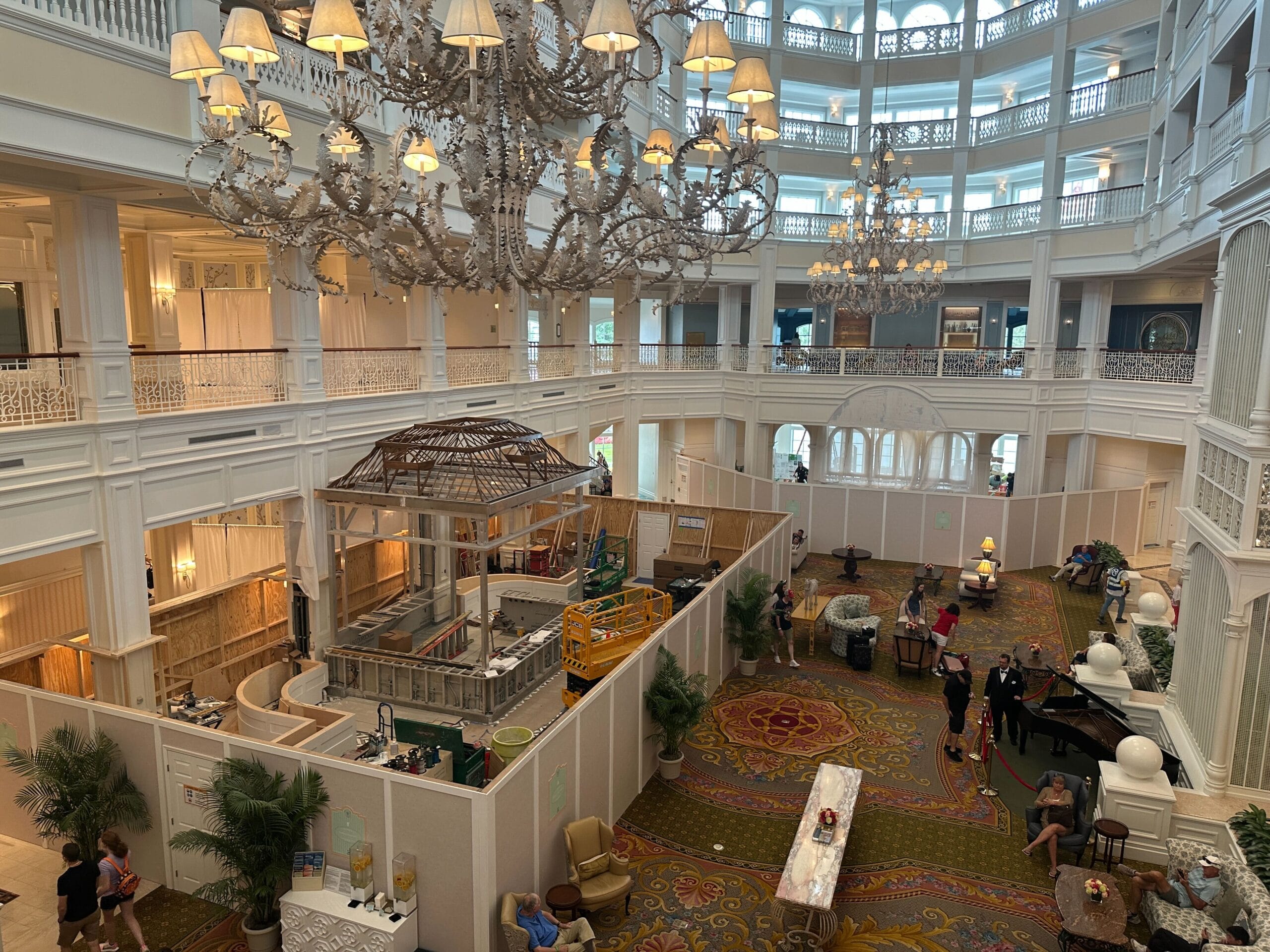 Grand hotel lobby with construction barriers, chandeliers, and guests seated or walking through the space.