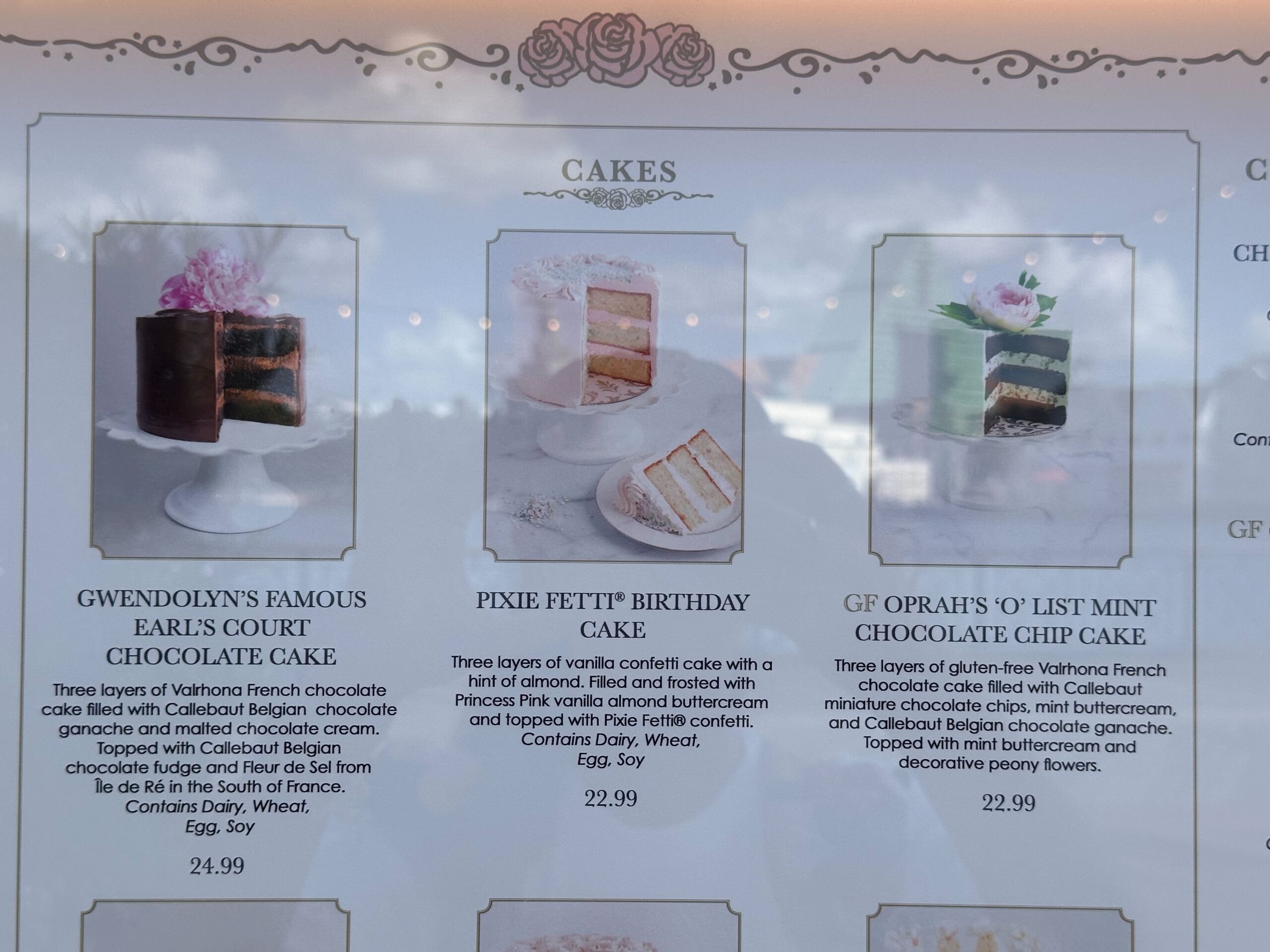 A menu from our cake bake shop showcasing three delightful options: Gwendolyn's Chocolate Cake, Pixie Petit Birthday Cake, and Oprah's Mint Chocolate Chip Cake, each complete with a tempting description and price.