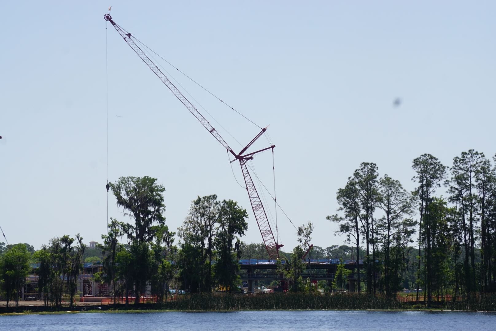 A large red crane looms behind the trees near a body of water, with the Disney Lakeshore Lodge construction site visible in the background.