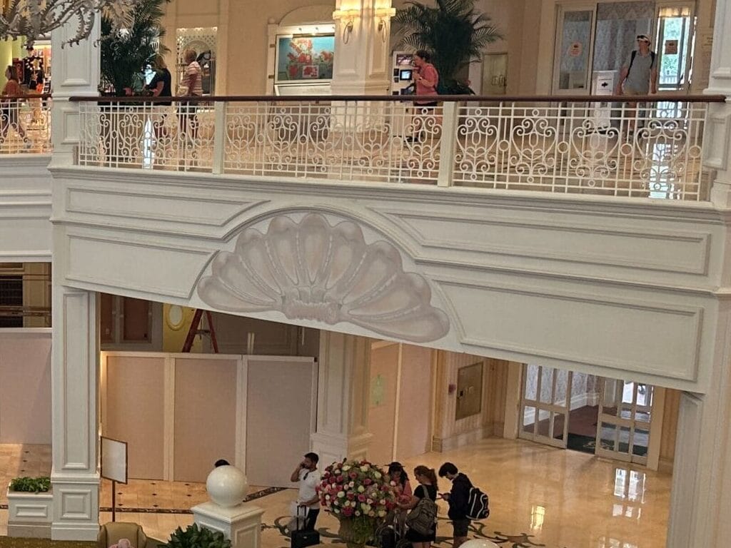 Elegant hotel lobby with chandelier, seating areas, plants, and construction barriers on the lower floor.
