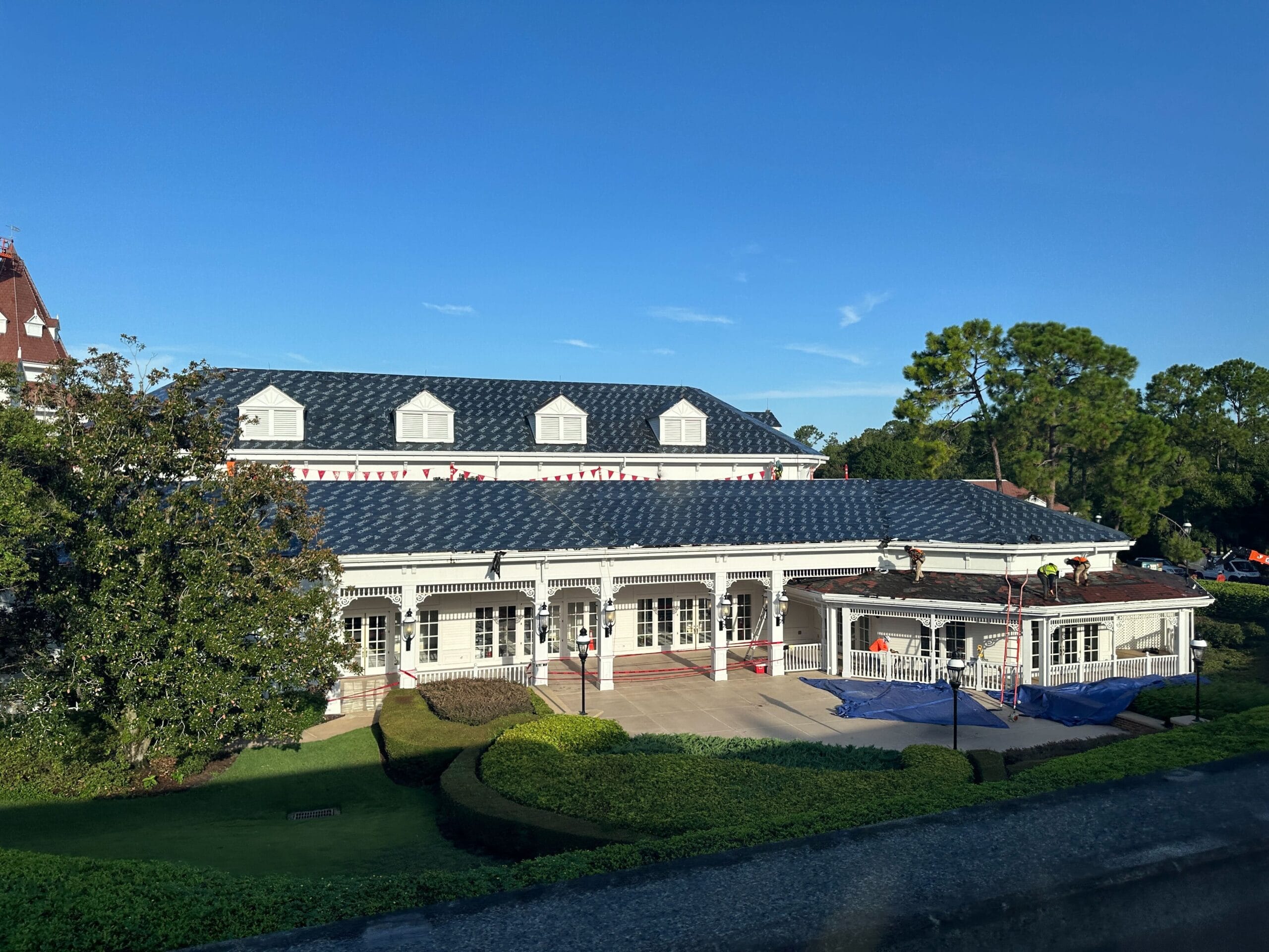 Convention center building with roof shingles removed, surrounded by greenery, under a clear blue sky.