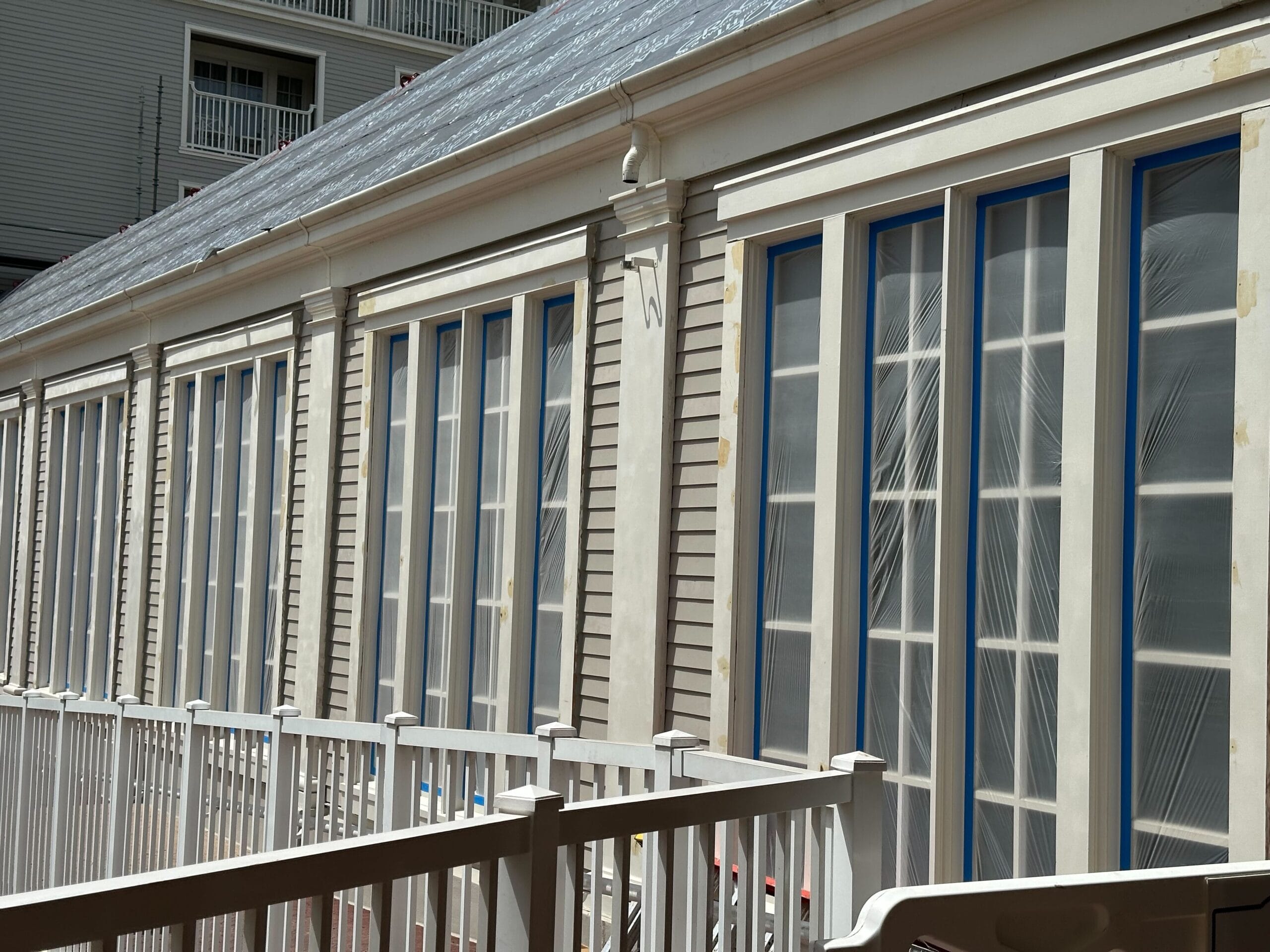 A row of white-framed French doors with blue-taped outlines stands behind a white railing. Scaffolding hints at ongoing renovations on the building's beige siding, seamlessly blending into the nautical charm of Disney's Yacht Club.