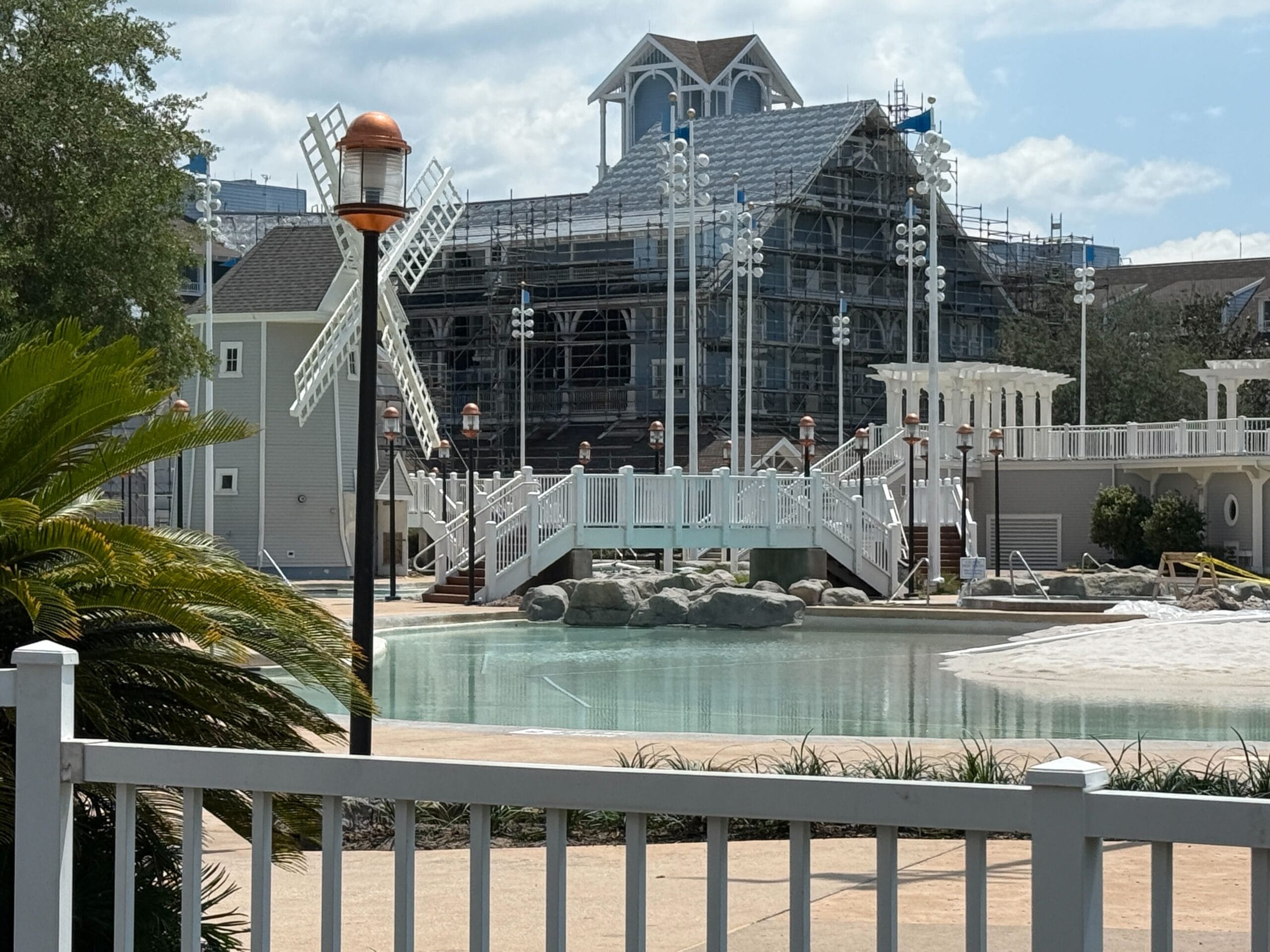 A pool area with a white bridge, windmill structure, and a building under construction in the background.