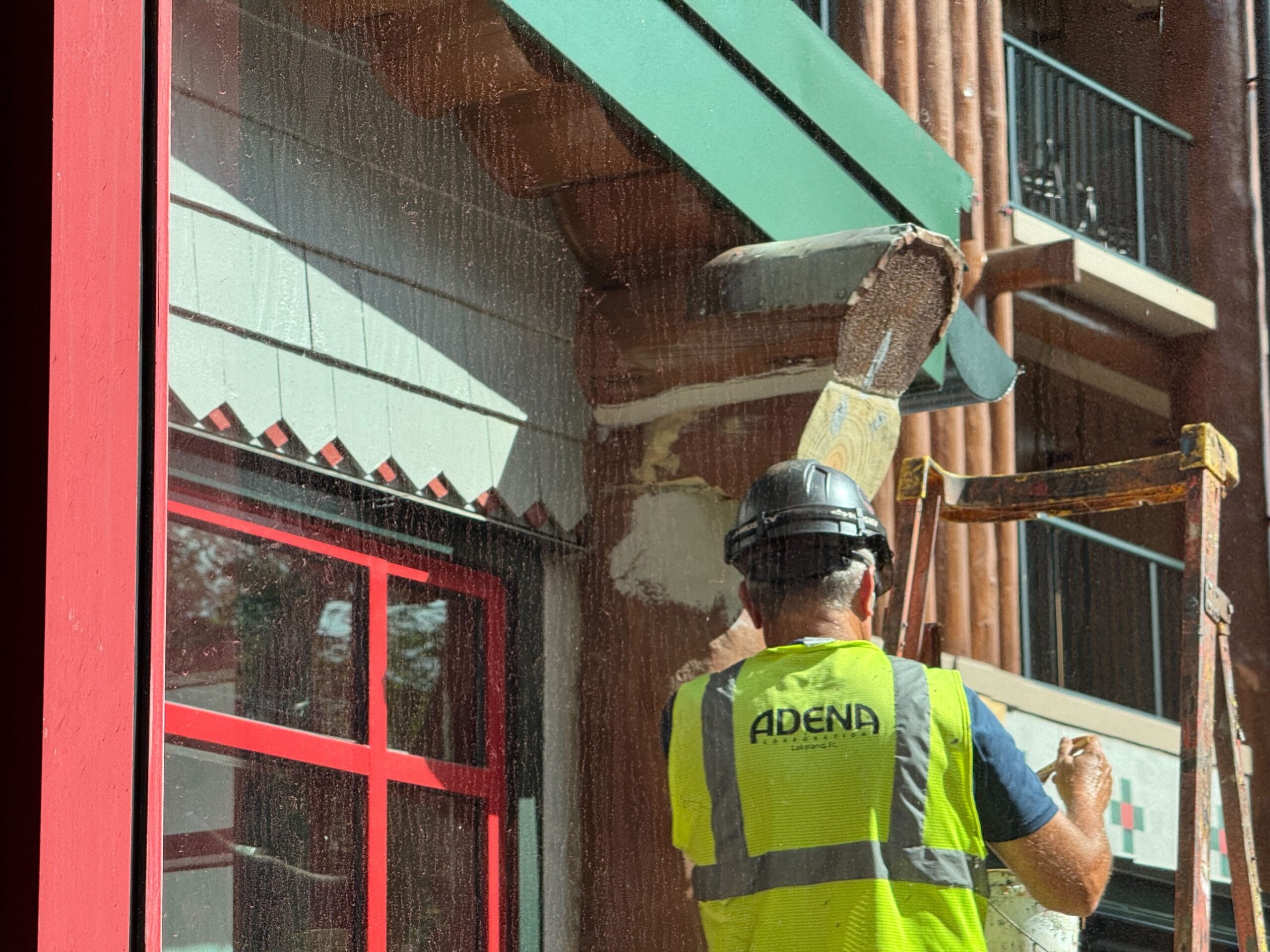 A construction worker in a safety vest and helmet operates a lift near a building facade under renovation.