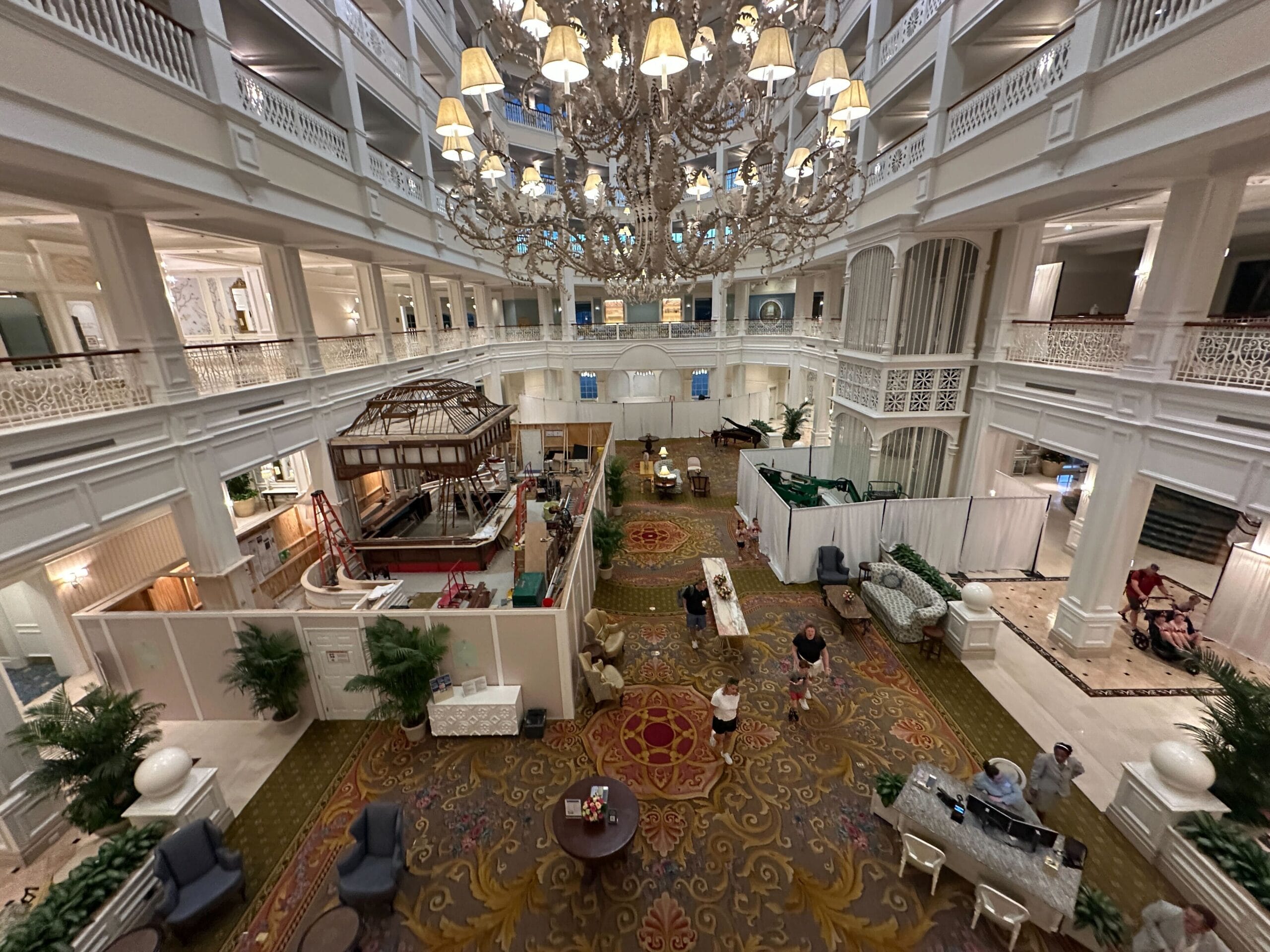 Grand hotel lobby with a large chandelier, elegant decor, people seated, and construction barriers in the center.