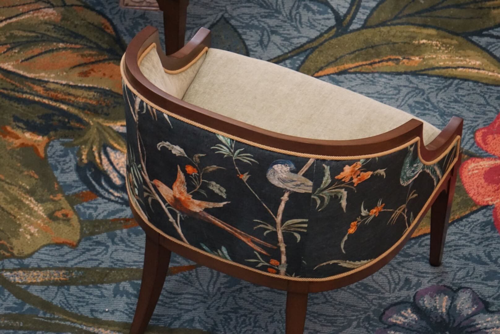 A wooden chair styled after Disney’s Grand Floridian Resort, with bird and floral upholstery like park lobby decor, dark backdrop.