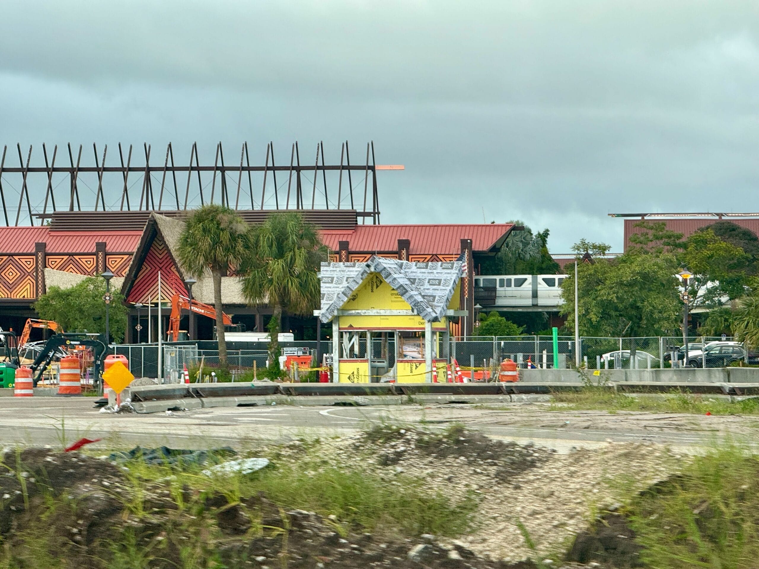 A small yellow building under construction near a hotel with a monorail passing in the background.