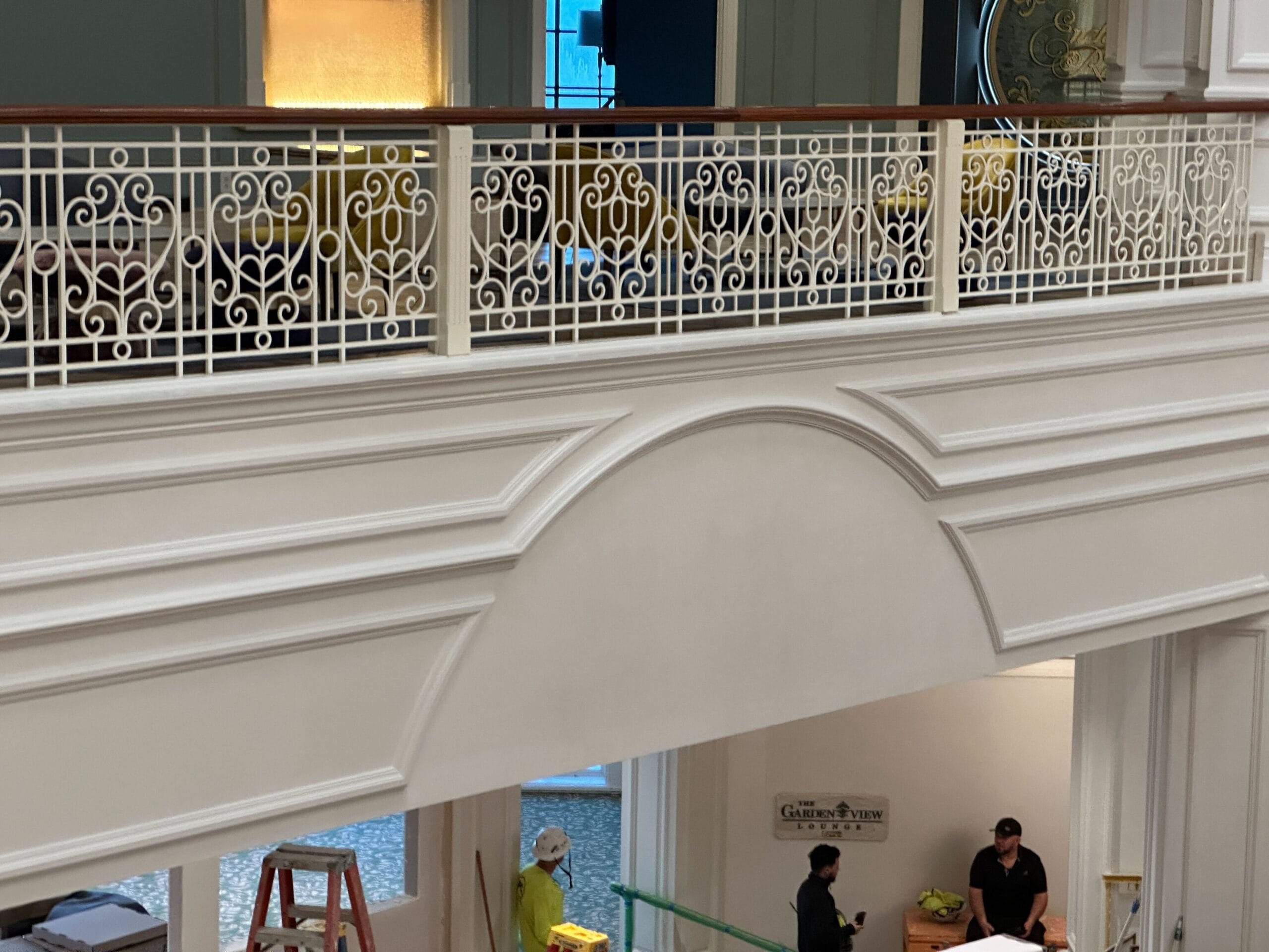 Workers in a hotel lobby with ornate white railings, reminiscent of the Grand Floridian, and people below working.