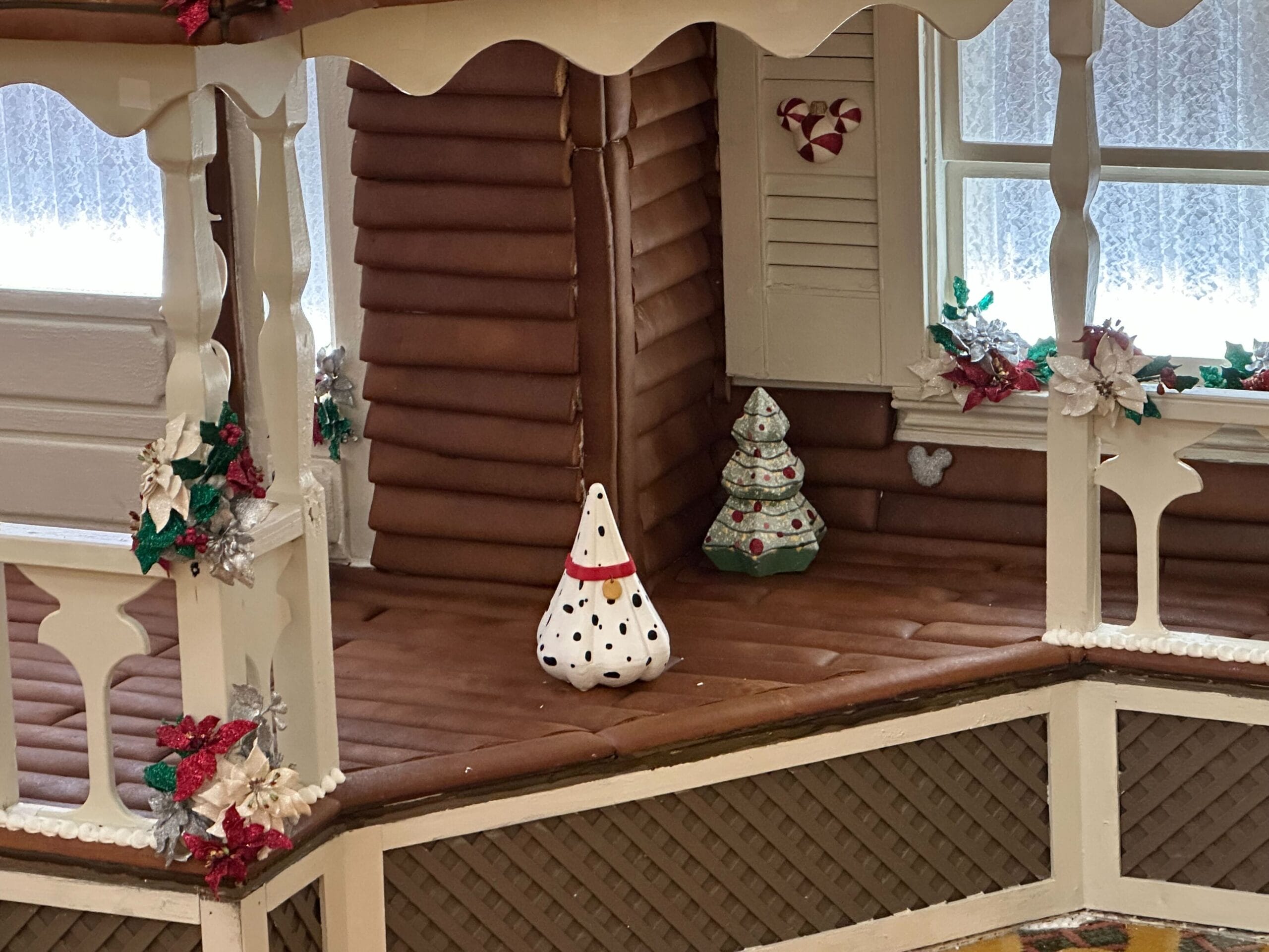 A gingerbread house porch with festive decorations, including a spotted cone ornament and small Christmas trees.