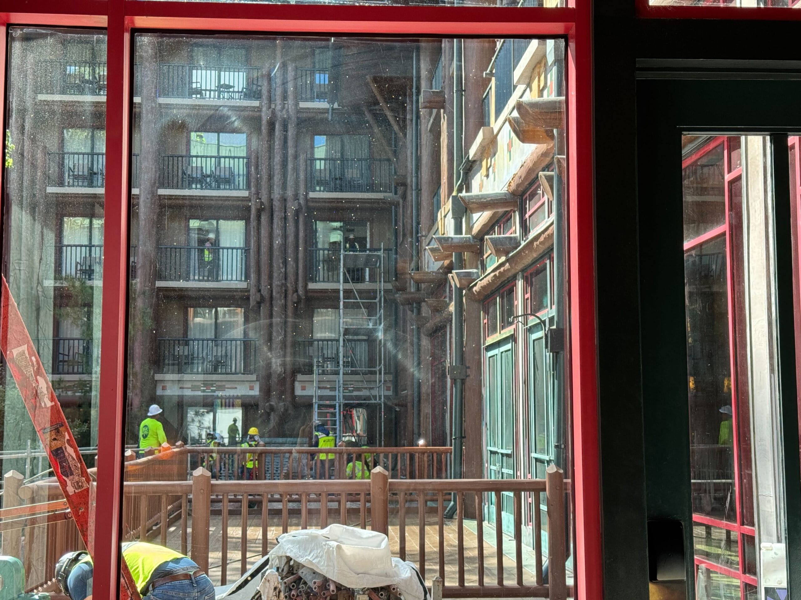 View through a window of construction workers and scaffolding outside a multi-story building with balconies.